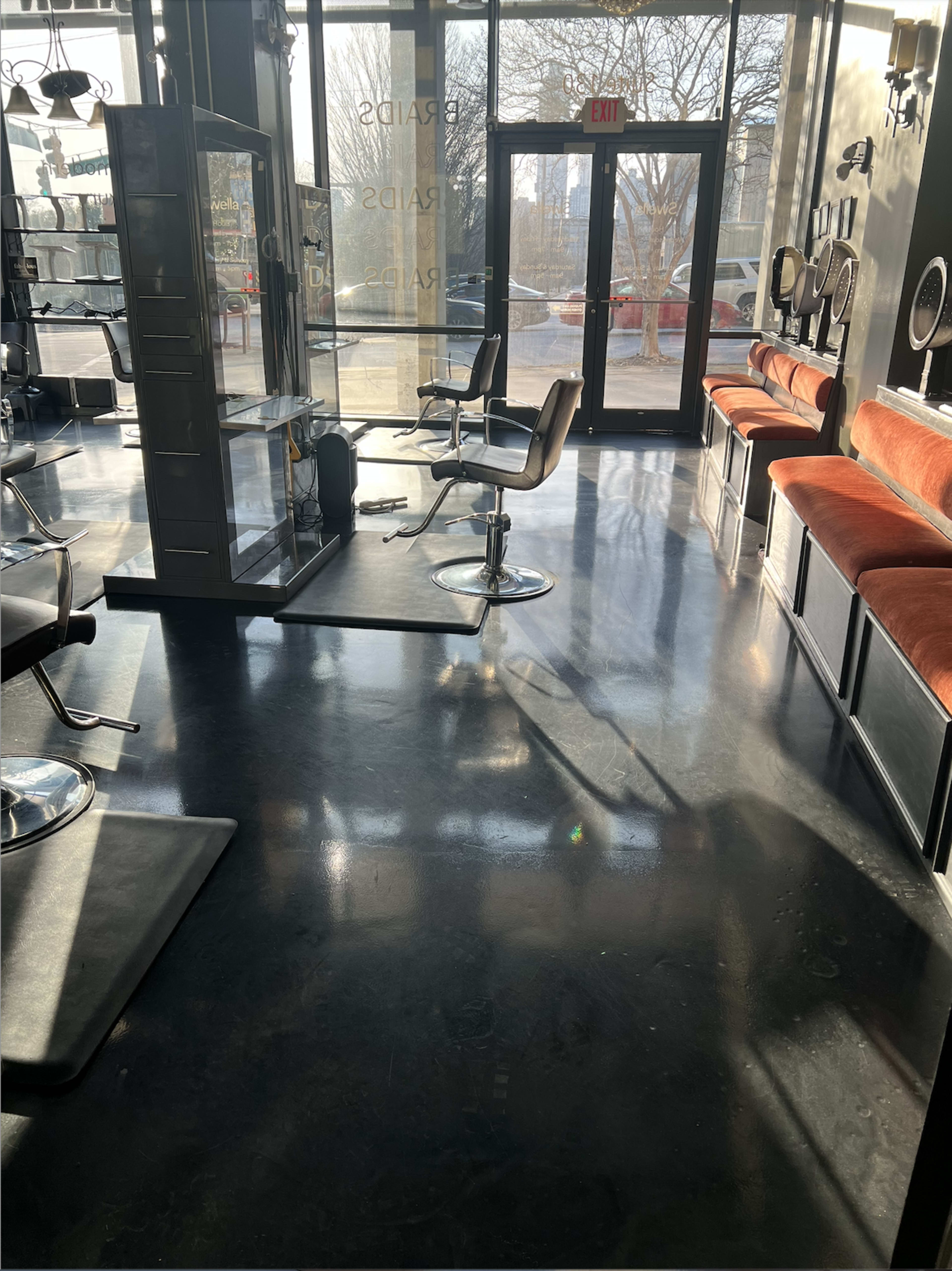 The interior of a hair salon features modern chairs, salon mirrors, and large windows allowing natural light to fill the space.