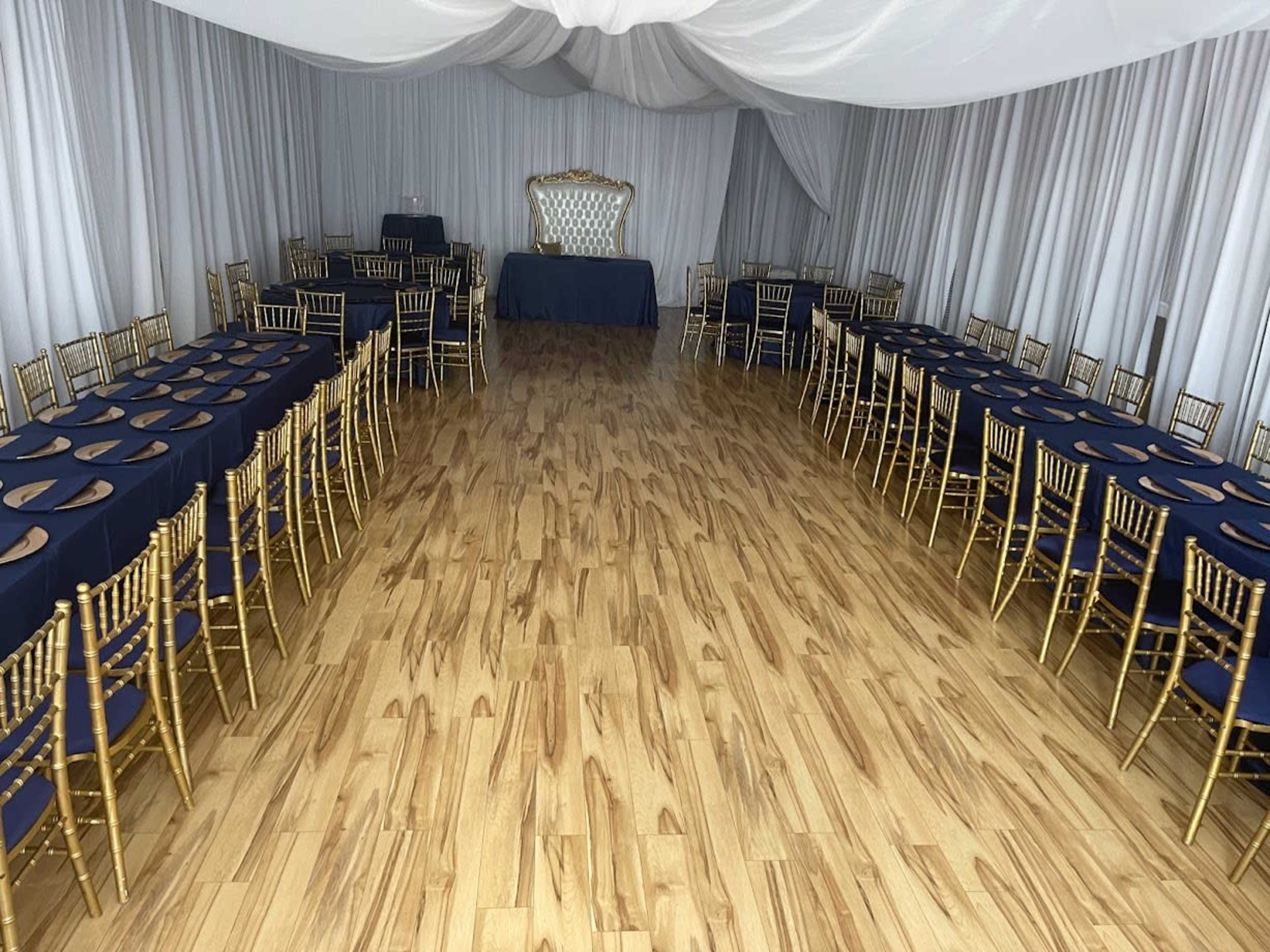 The image shows a banquet hall set up with rows of tables covered in dark blue cloths and surrounded by gold chairs.