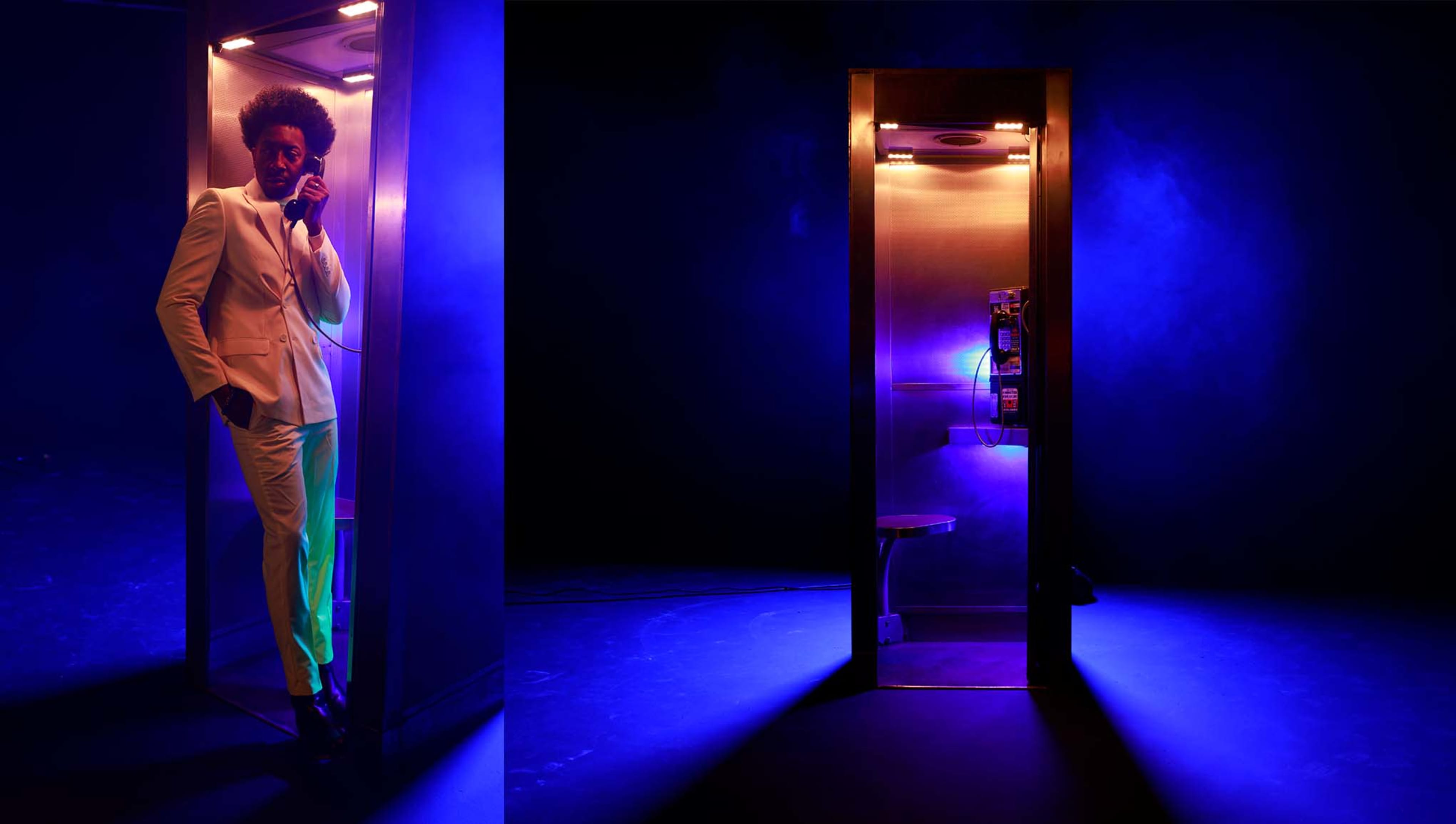 A person in a white suit stands inside a lit telephone booth with purple lighting against a dark background.