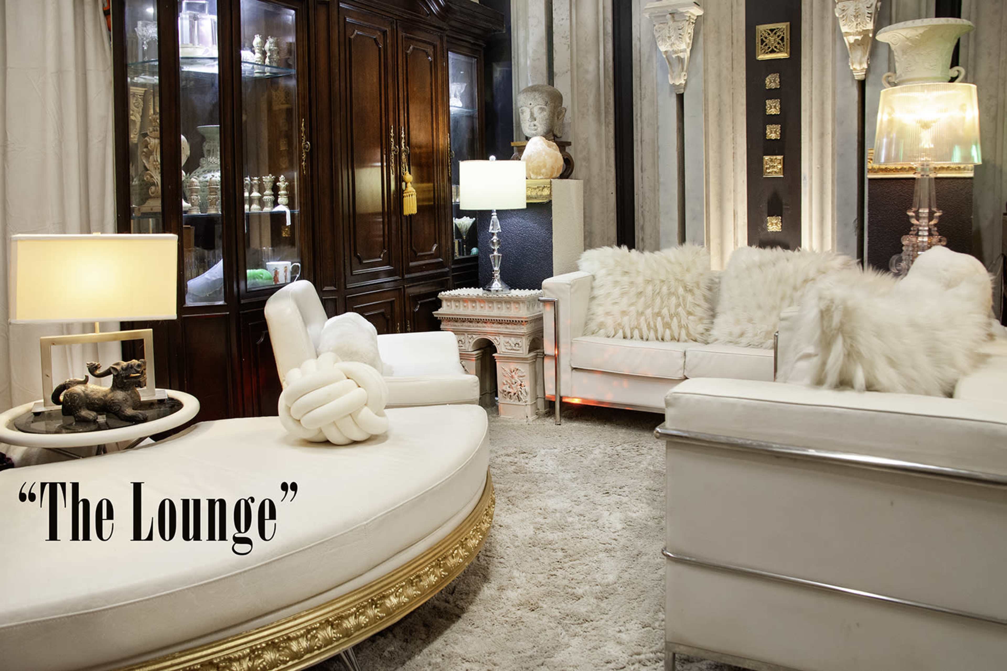 The image depicts a stylish lounge area featuring plush seating, decorative lamps, and ornate furniture against a softly lit backdrop.