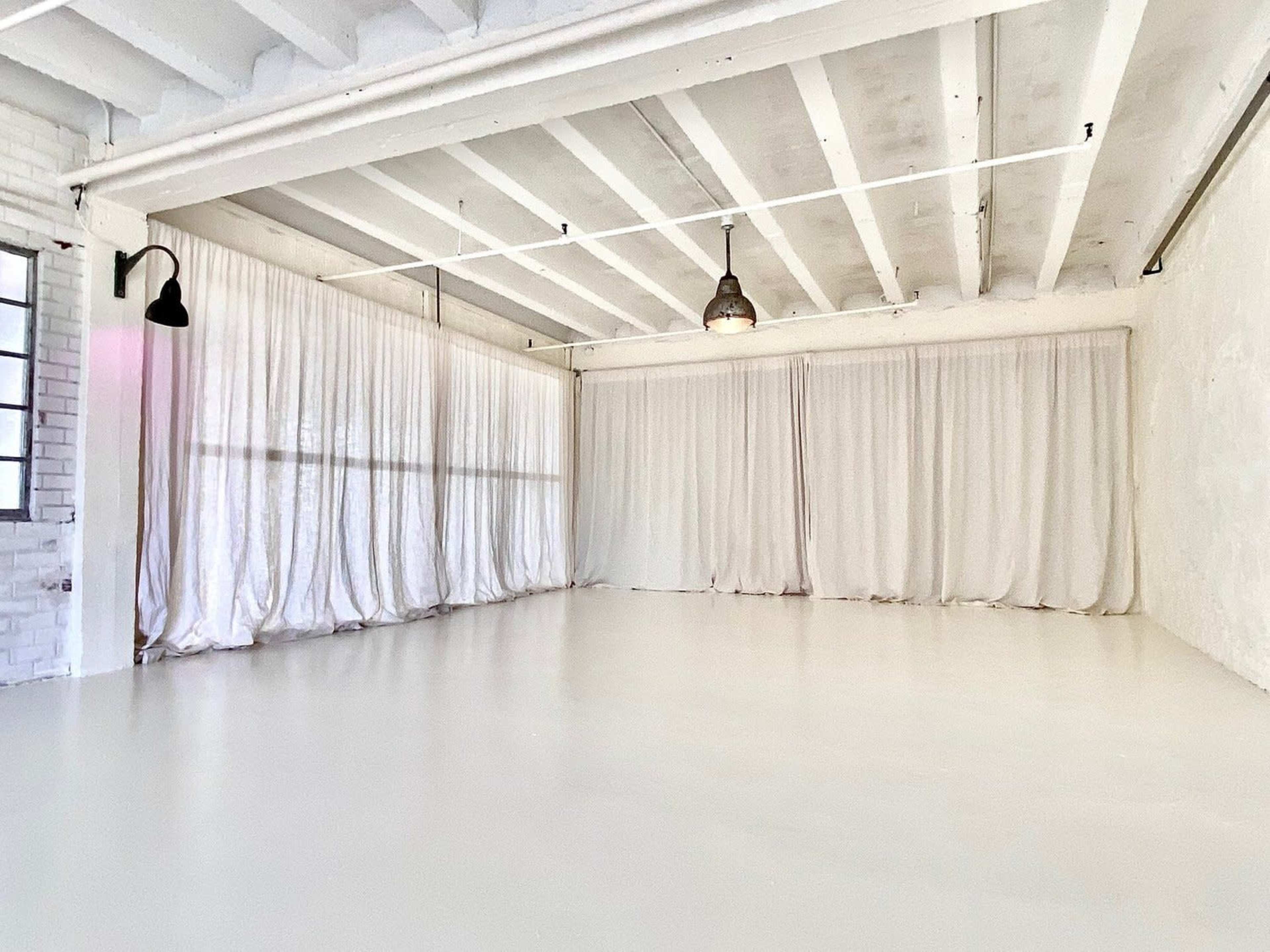 A spacious room with white walls, a polished floor, and large curtains covering the windows.