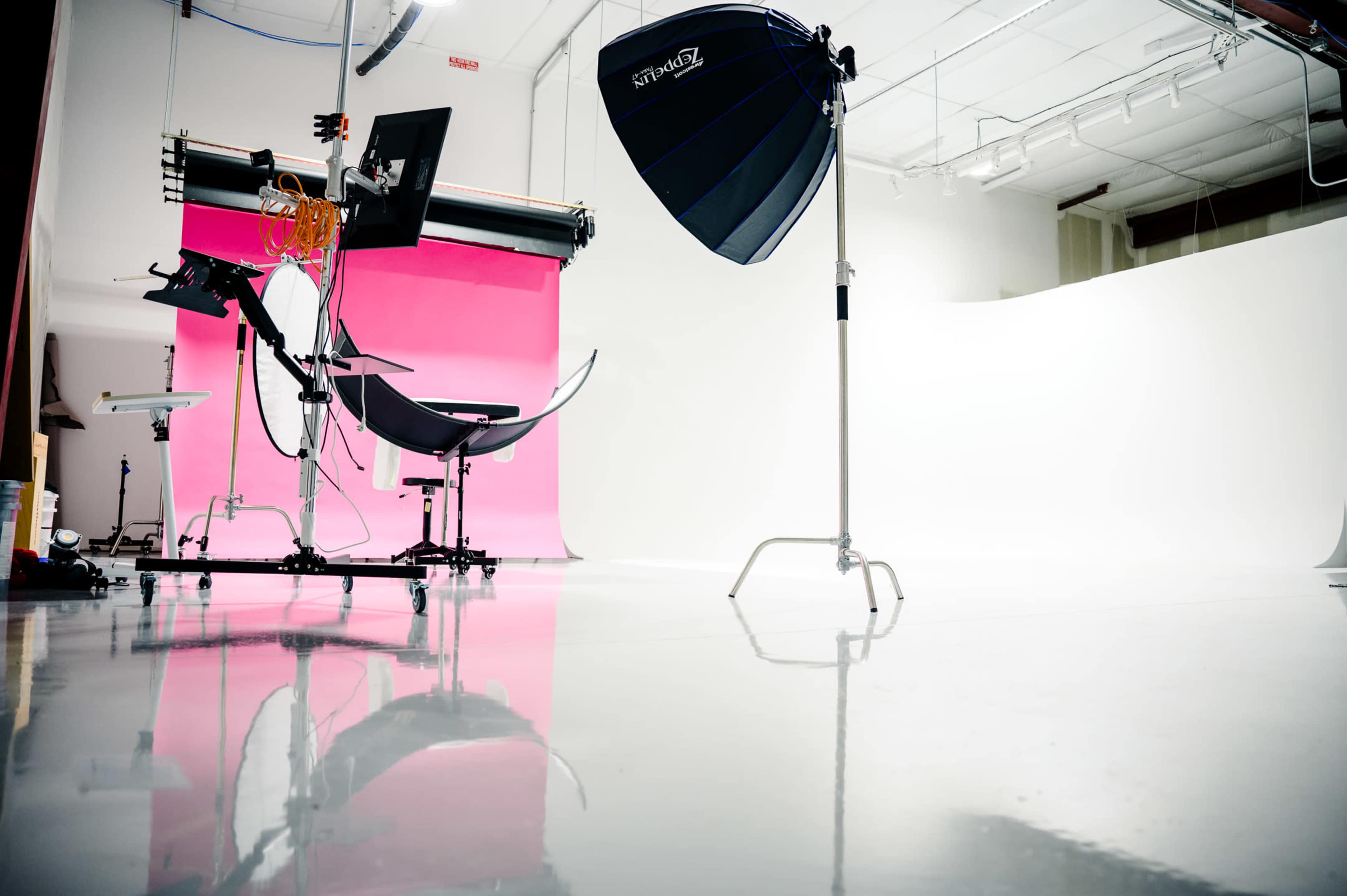 A photography studio with a pink backdrop, a large light umbrella, and equipment arranged on a shiny floor.