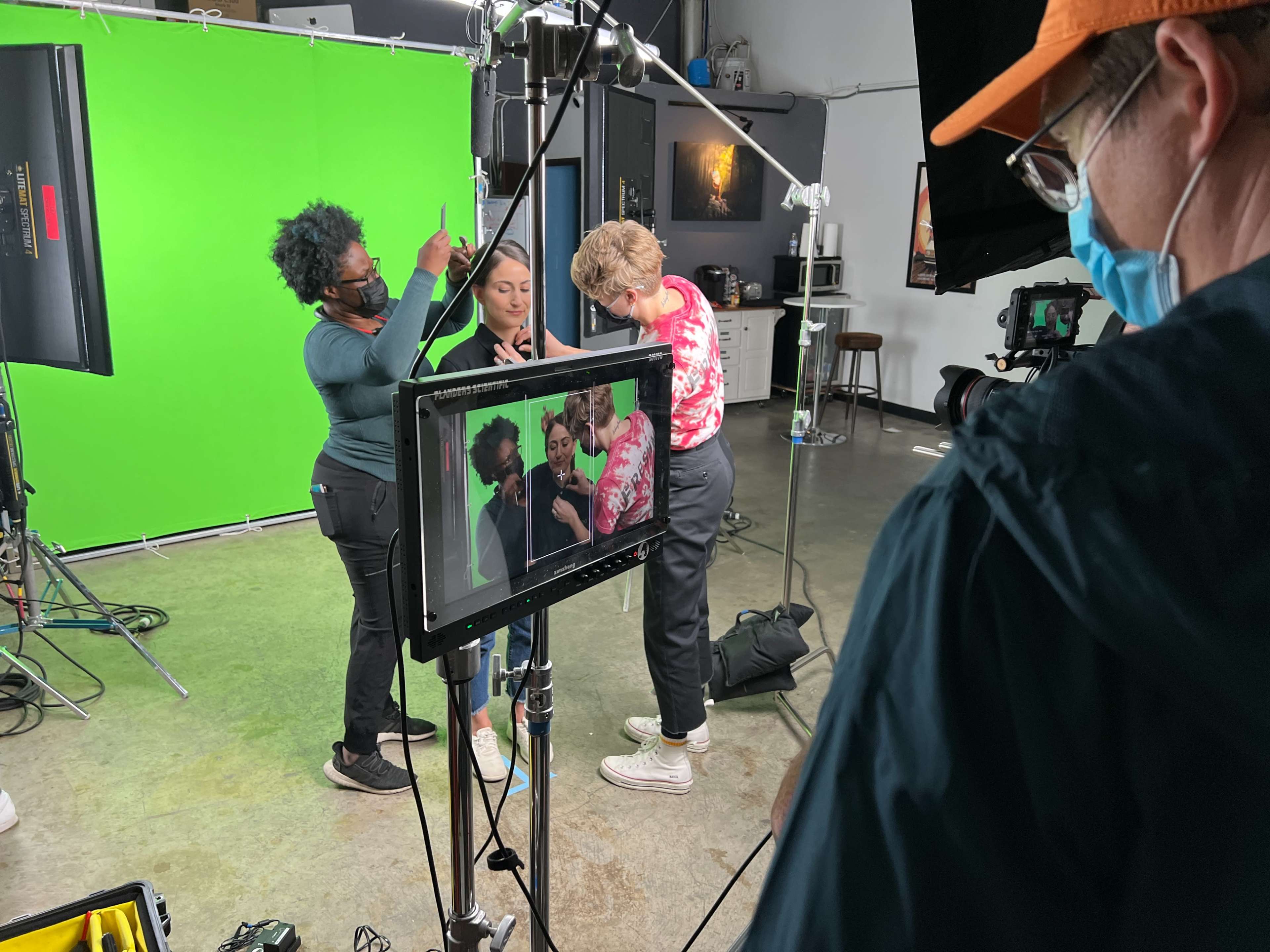 A group of four people are preparing for a shoot in front of a green screen, with cameras and equipment set up in a studio.