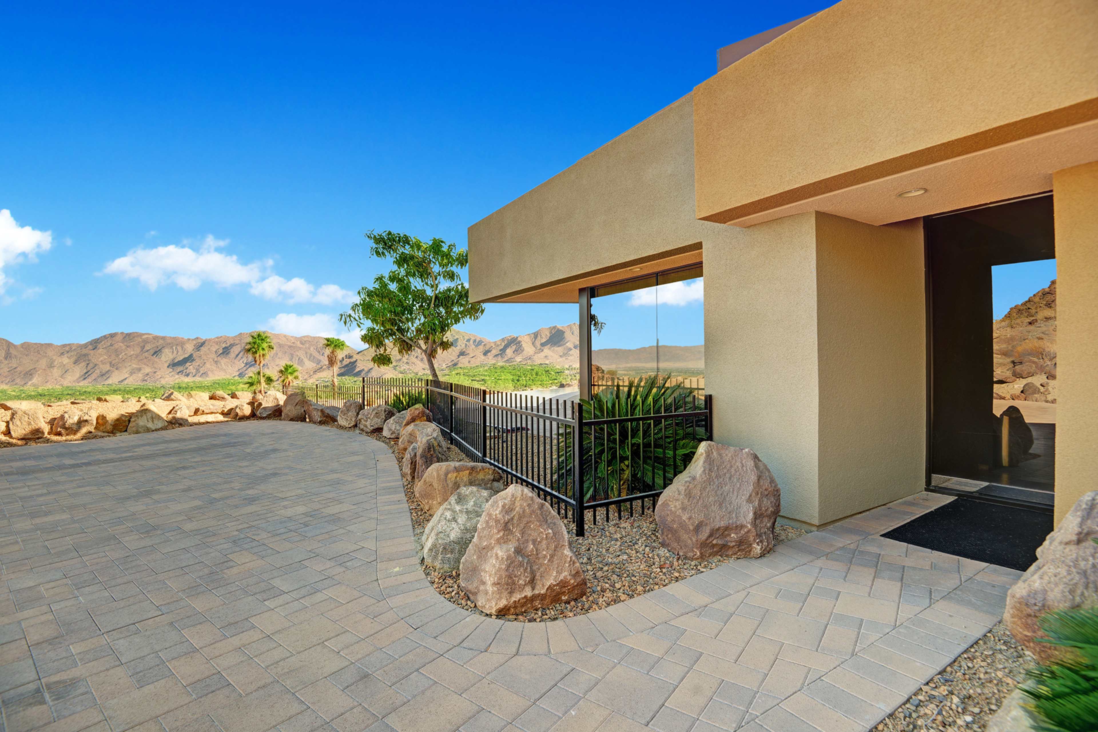 A modern building entrance with a paved walkway surrounded by large rocks and a clear view of mountains in the background.