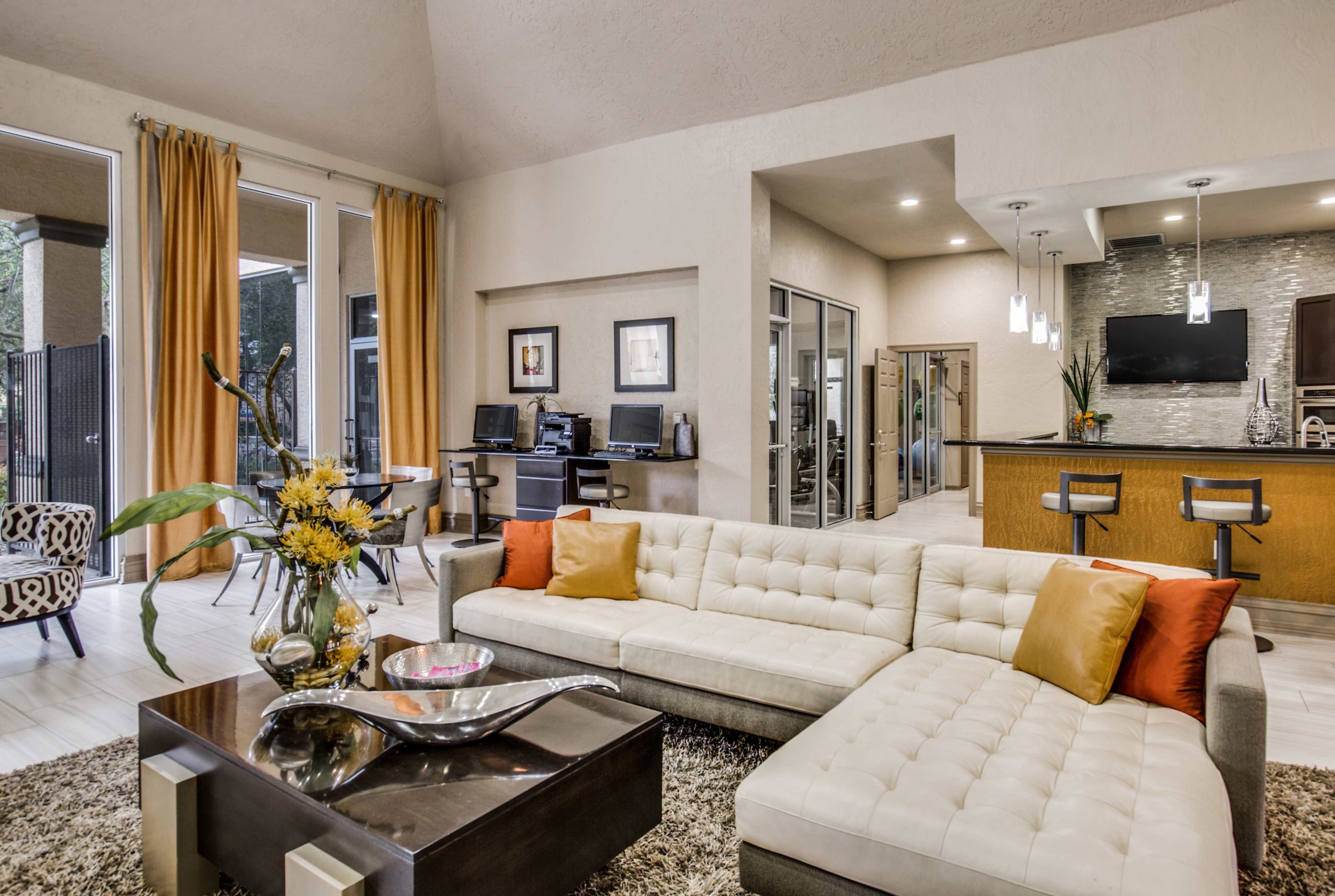 A modern living space featuring a sectional couch, a low table, and a kitchen area with bar seating.
