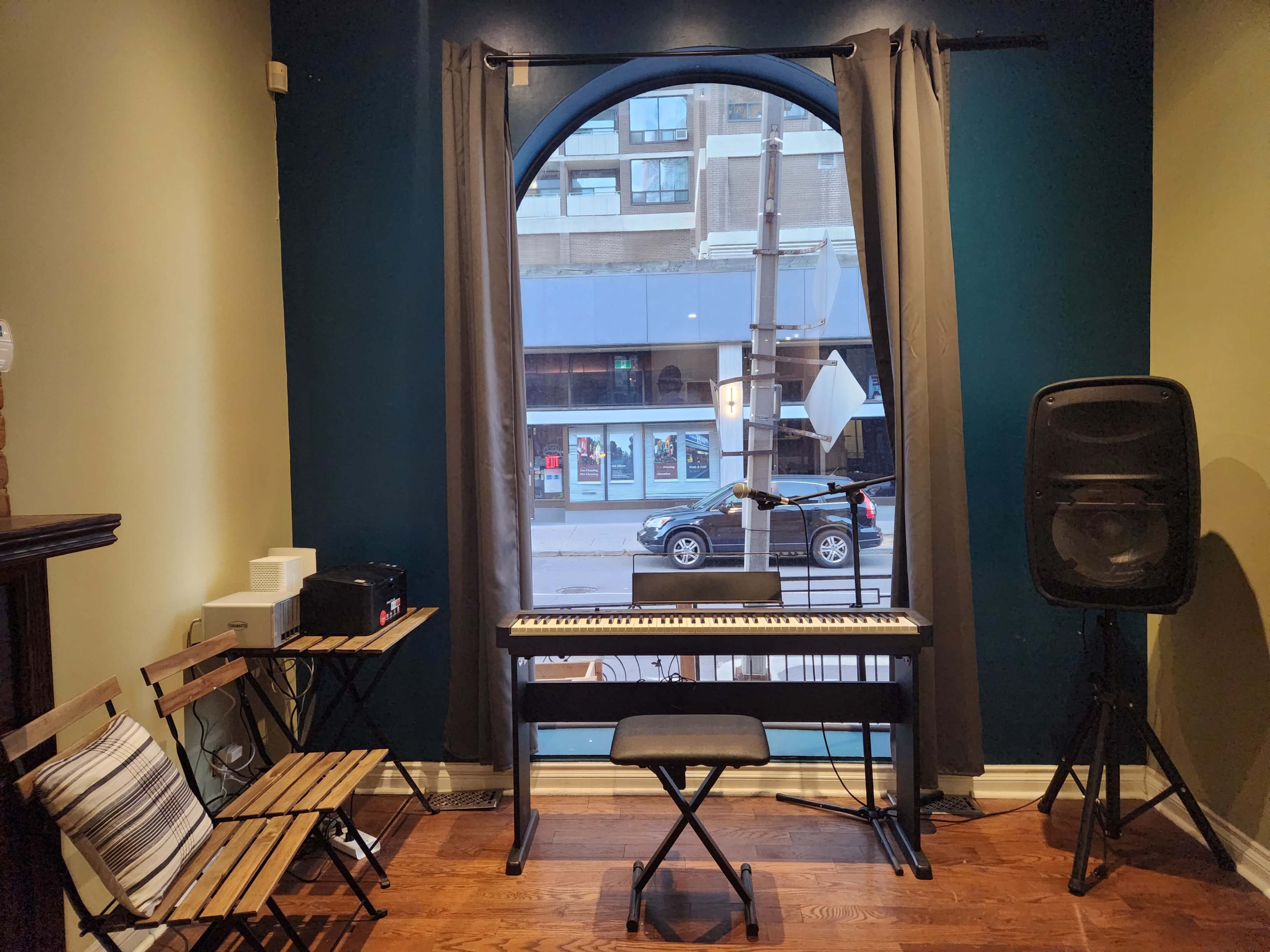 The scene shows a small room with a keyboard, a chair, and a speaker next to a large window overlooking a street.