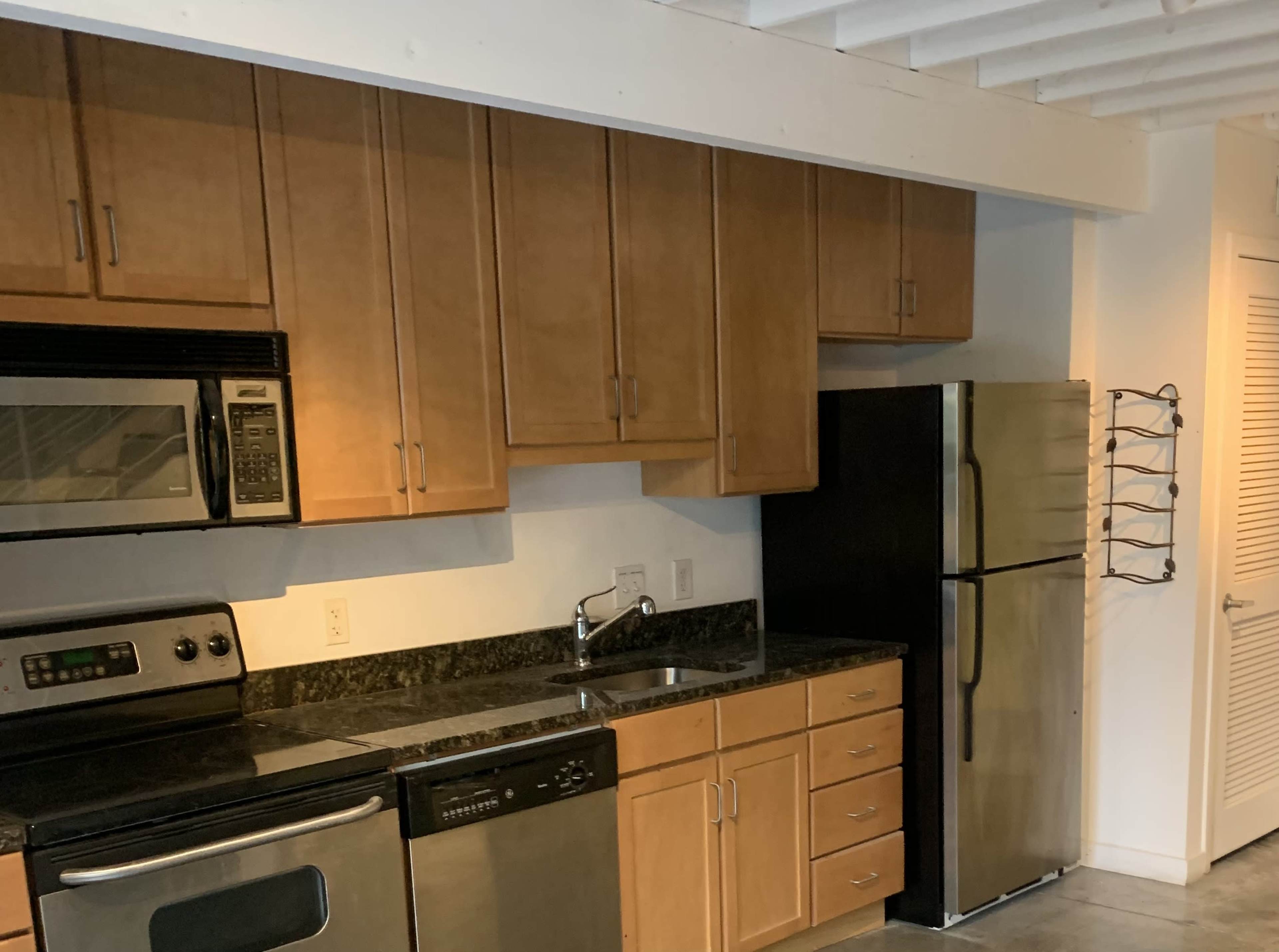 The image shows a kitchen with wooden cabinets, stainless steel appliances, and black granite countertops.