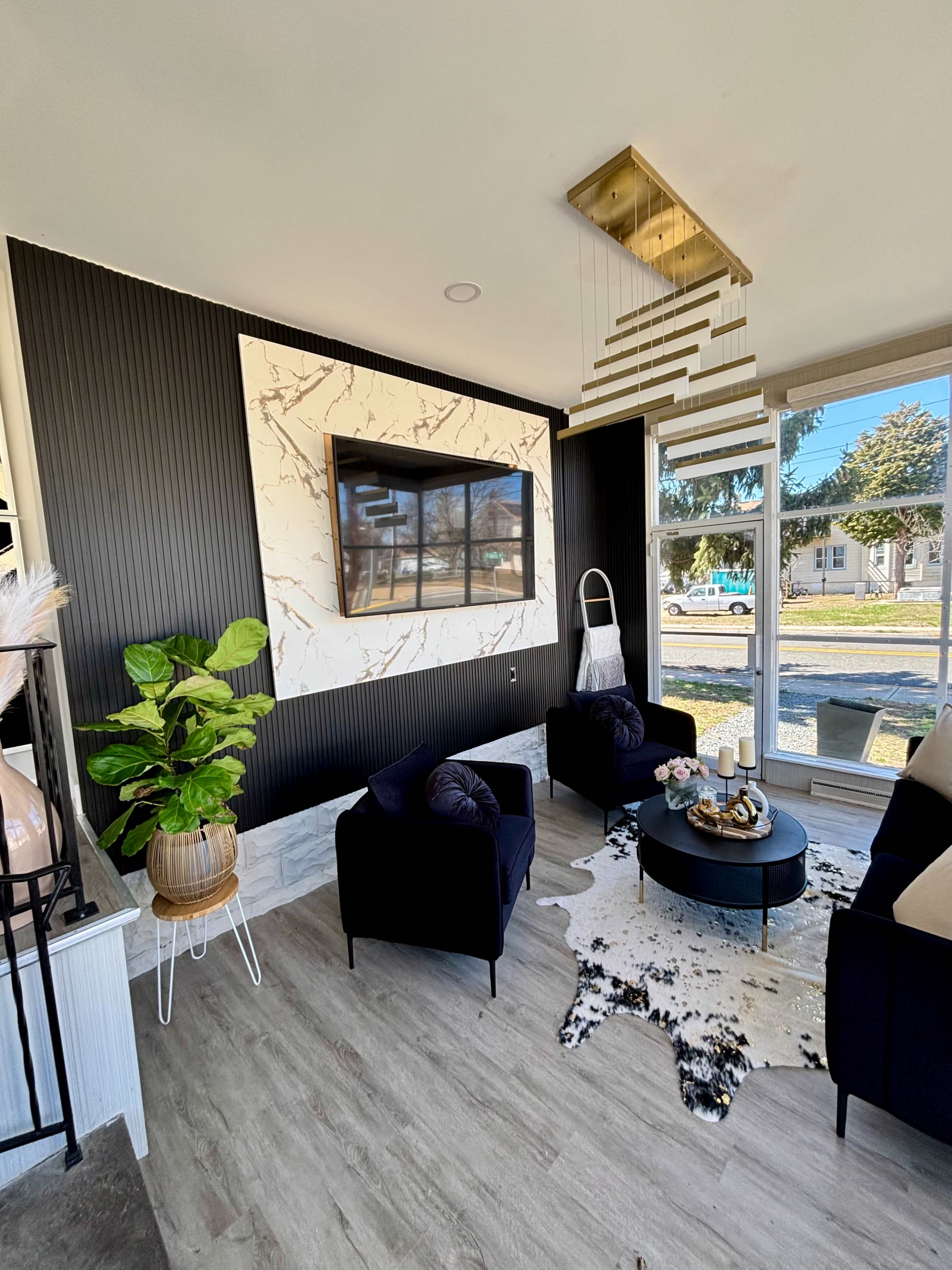 The image shows a modern living room with two black armchairs, a round coffee table, and a marble accent wall featuring a flat-screen TV.
