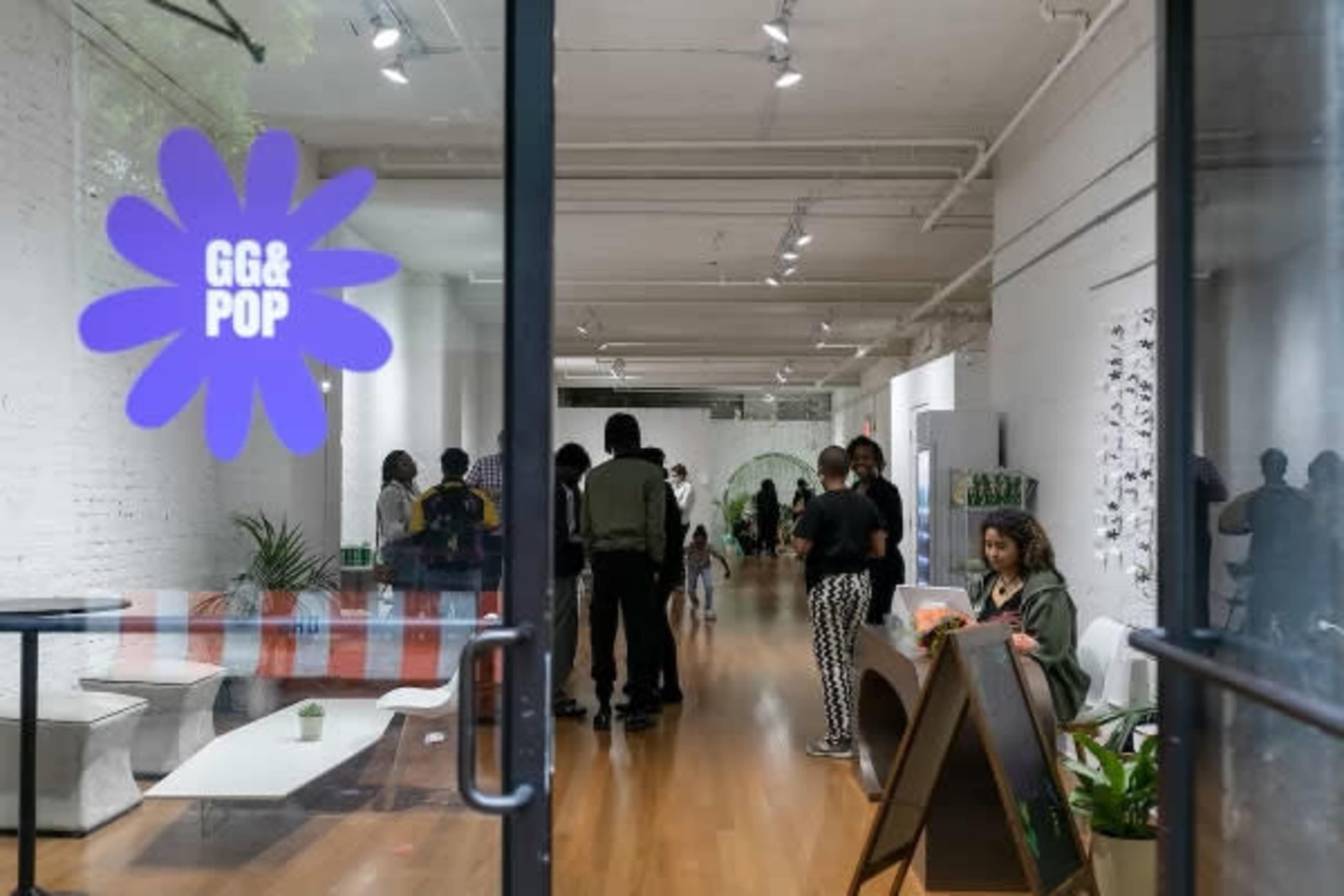 A bright, modern indoor space with a large window displaying the "GG & POP" logo and several people gathered inside, engaged in conversation.