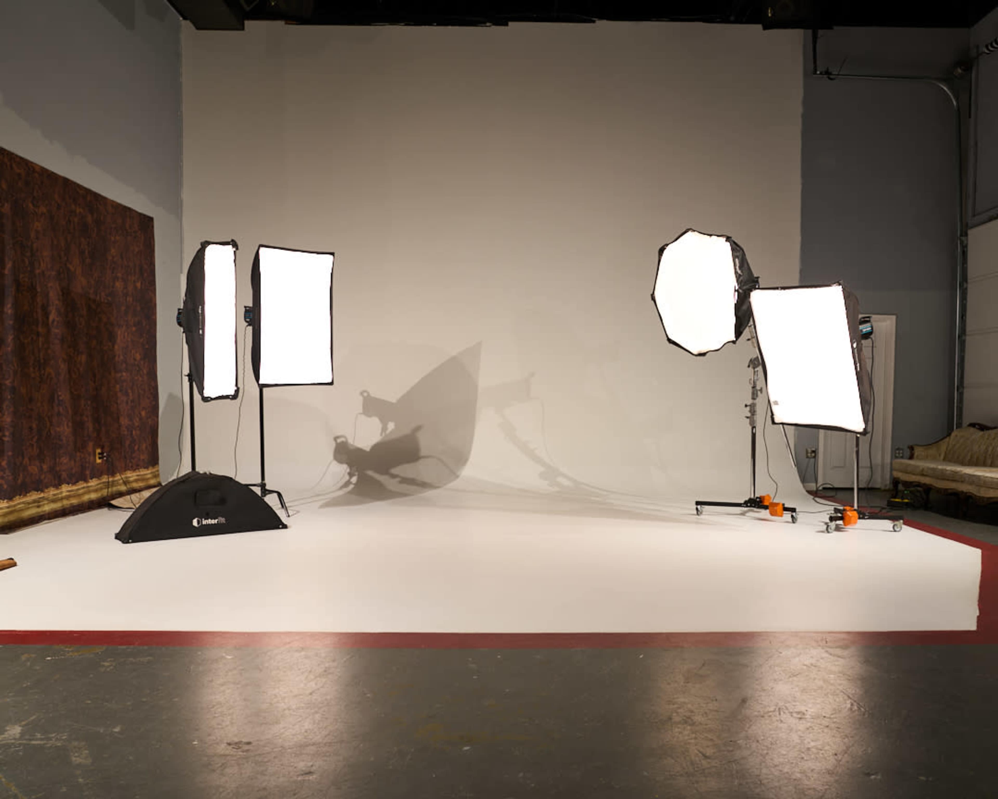A photography studio with three softbox lights positioned around a blank backdrop and a white floor.