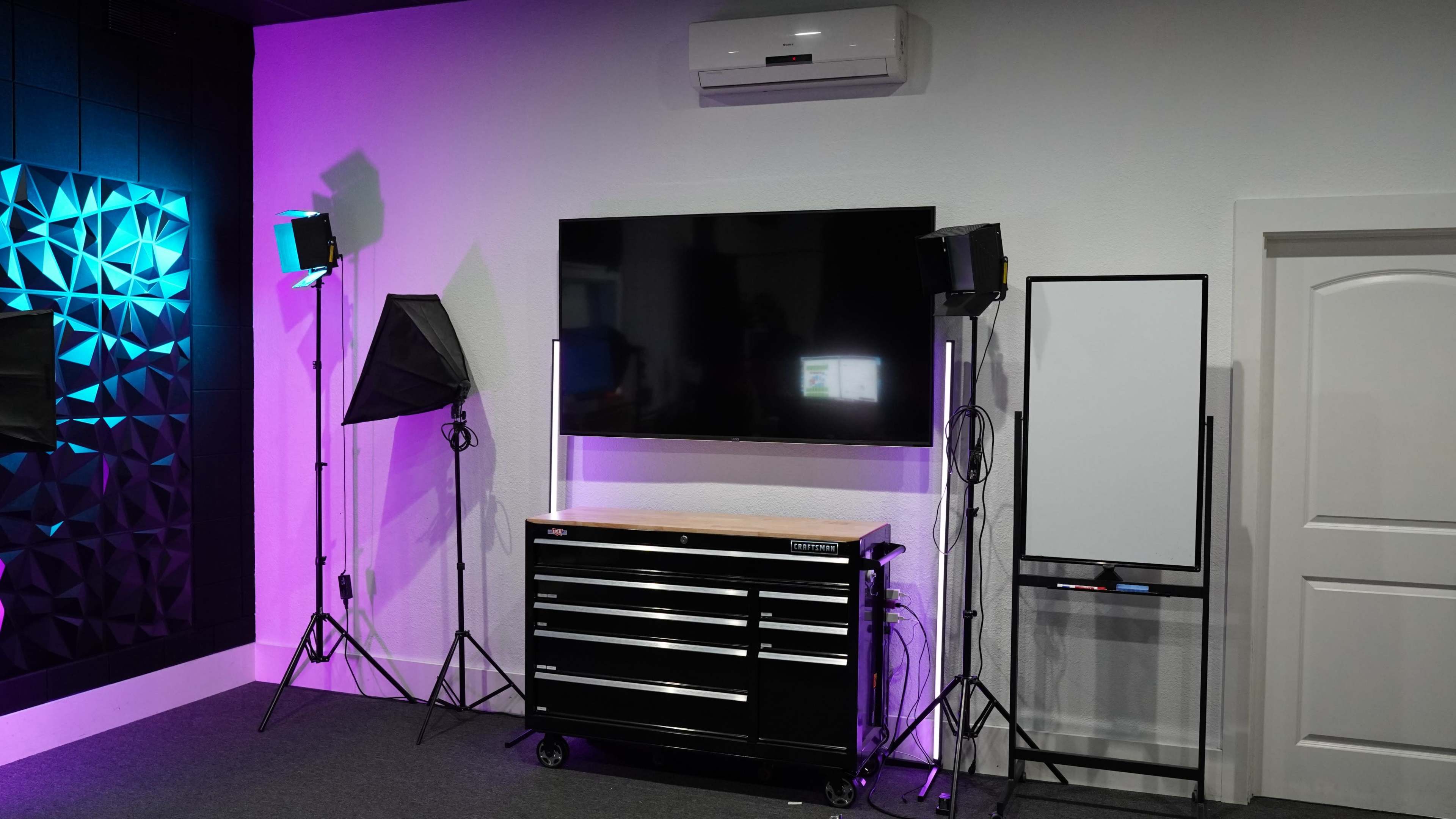A modern room featuring a black toolbox on wheels, a large flat-screen TV mounted on the wall, and studio lights arranged on stands.