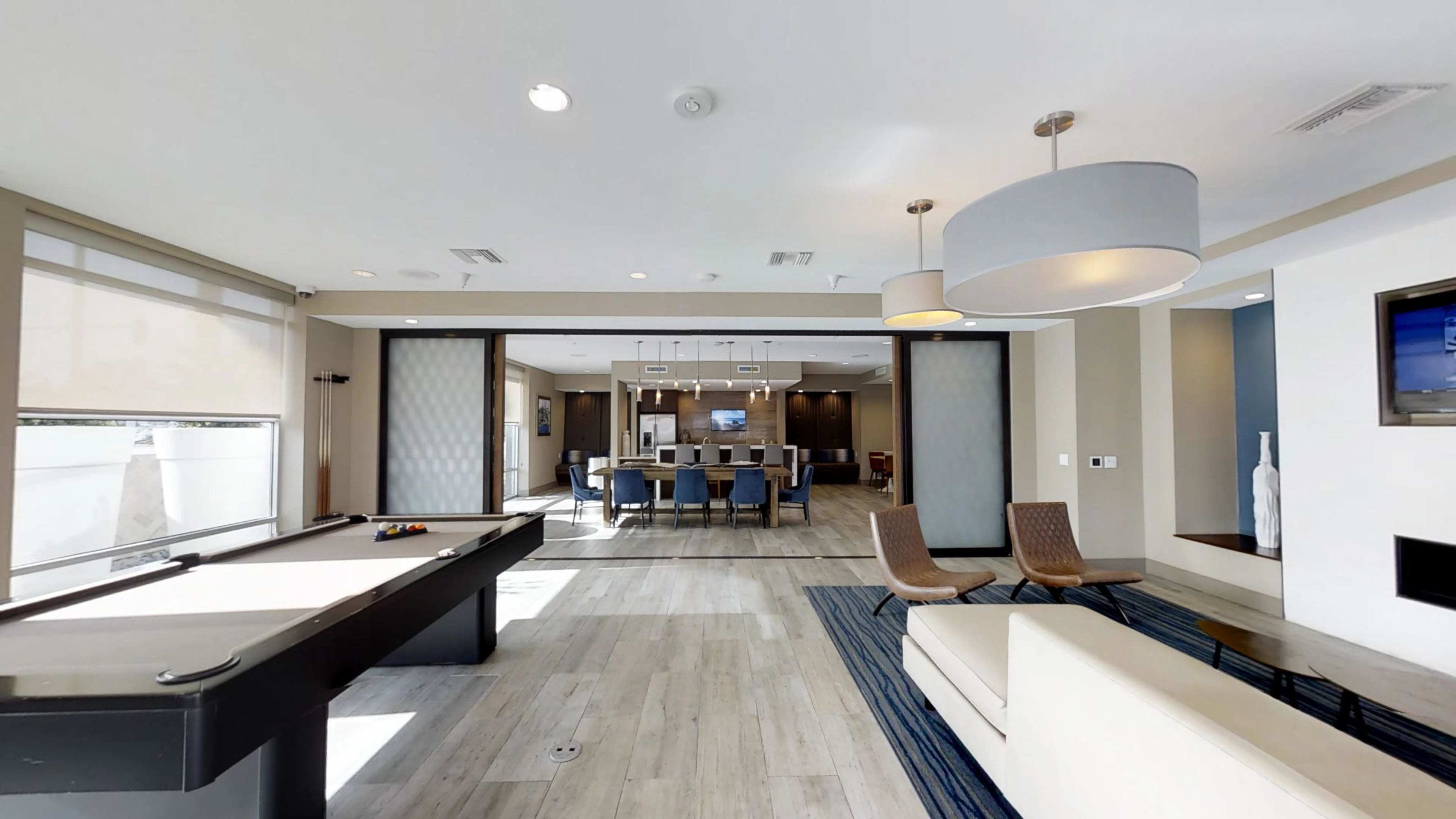 A modern lounge area featuring a pool table, seating, and a dining space in the background.