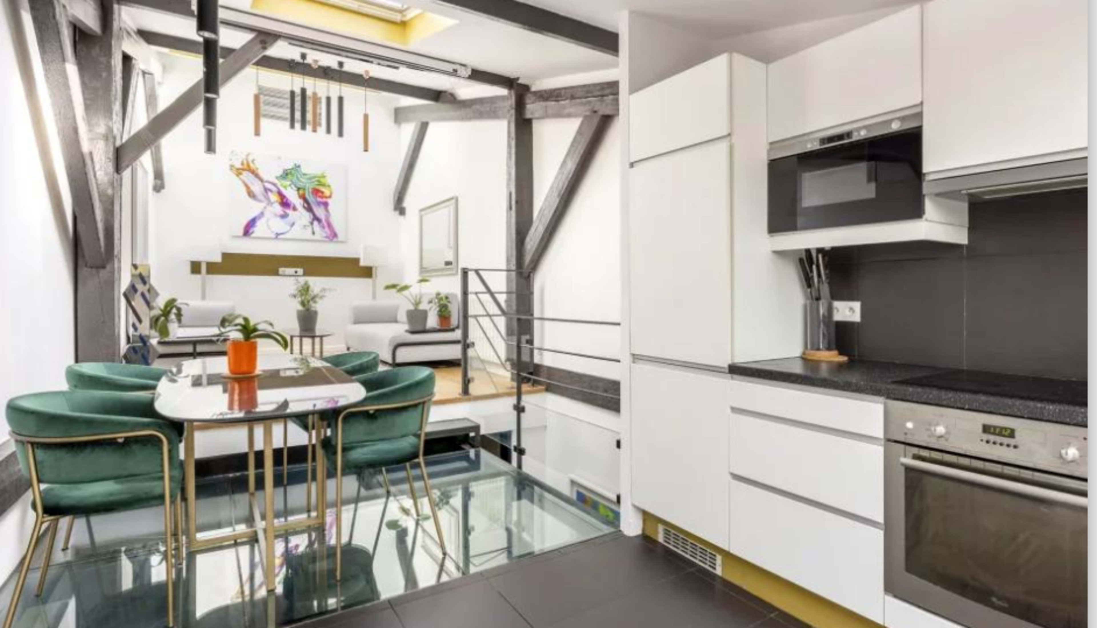 The image shows a modern kitchen adjacent to a dining area featuring a glass floor, with a living space visible in the background.