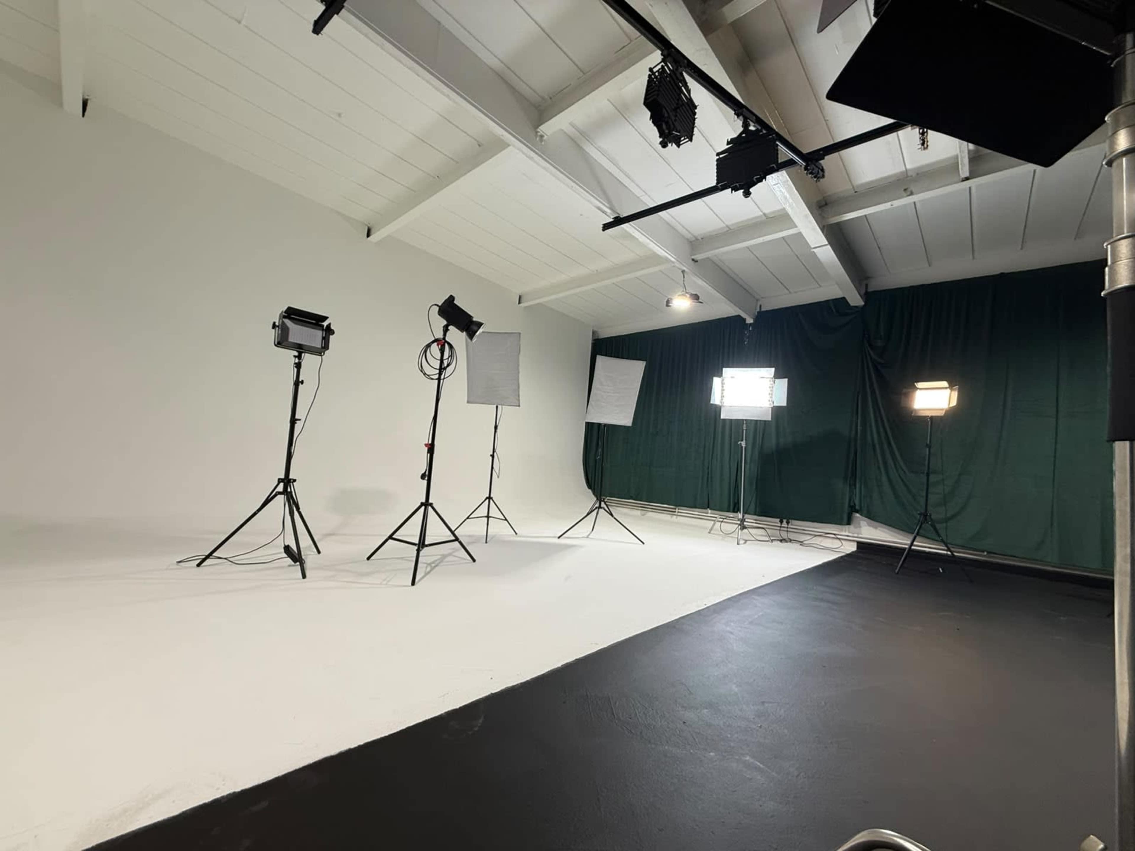 The image shows a spacious photography studio with various lighting equipment set up on the white floor.