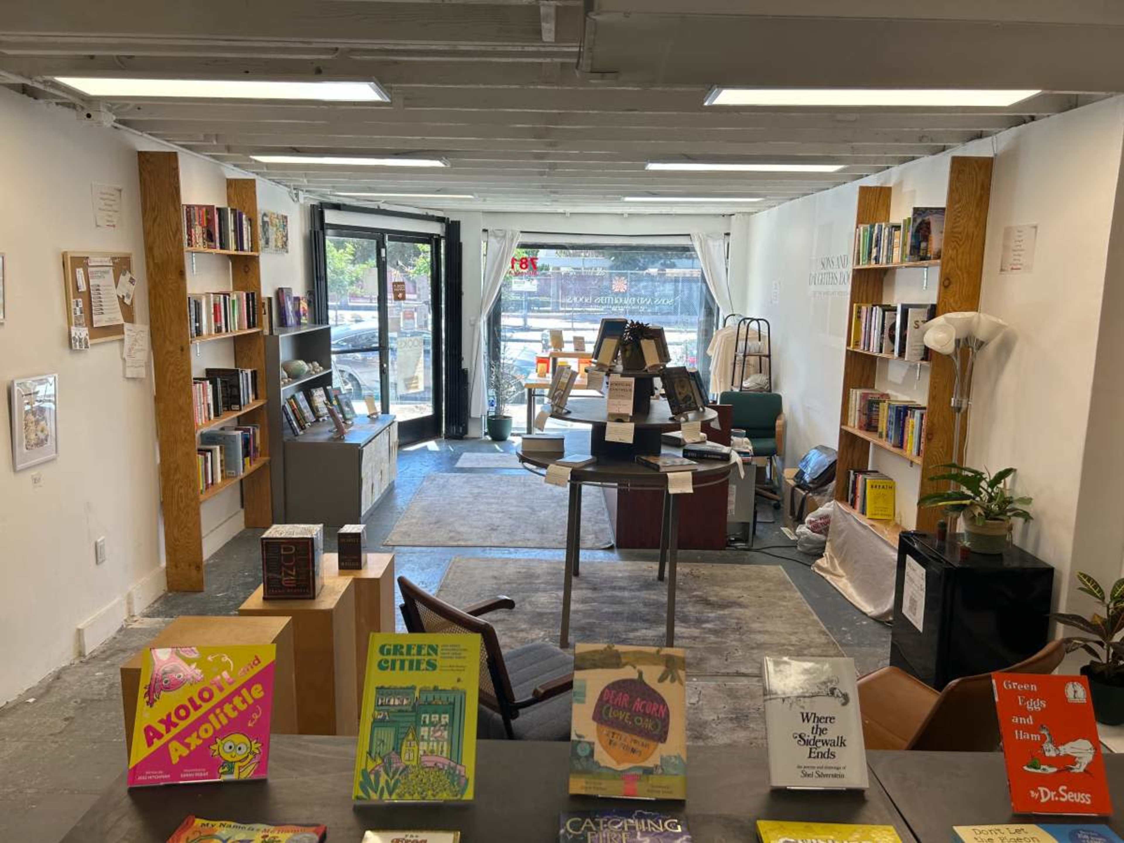 The image shows a bookstore interior with bookshelves lining the walls and a central display table featuring several books.