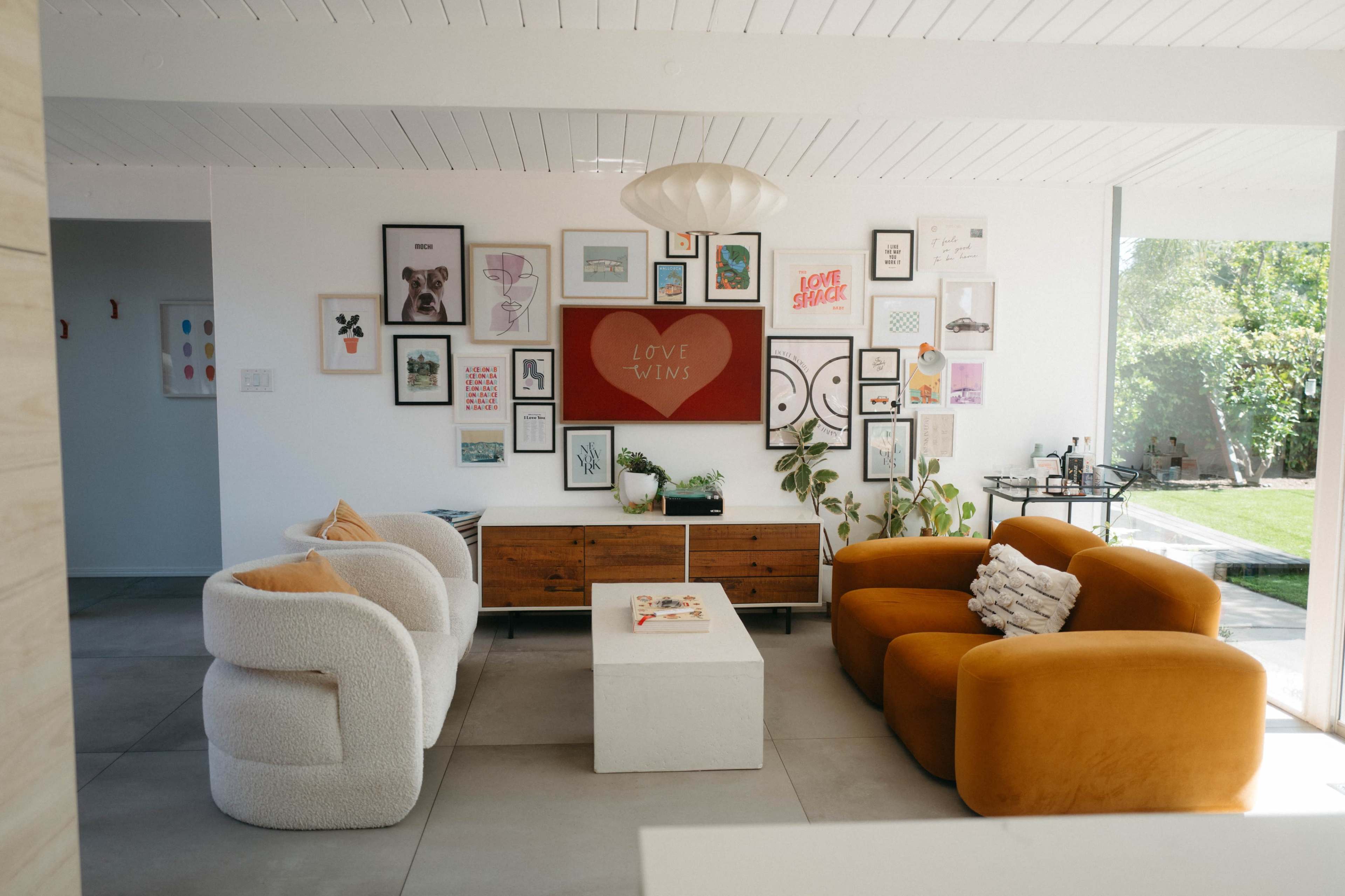 A modern living room features two colorful sofas, a wooden coffee table, and an array of framed artwork on the wall.
