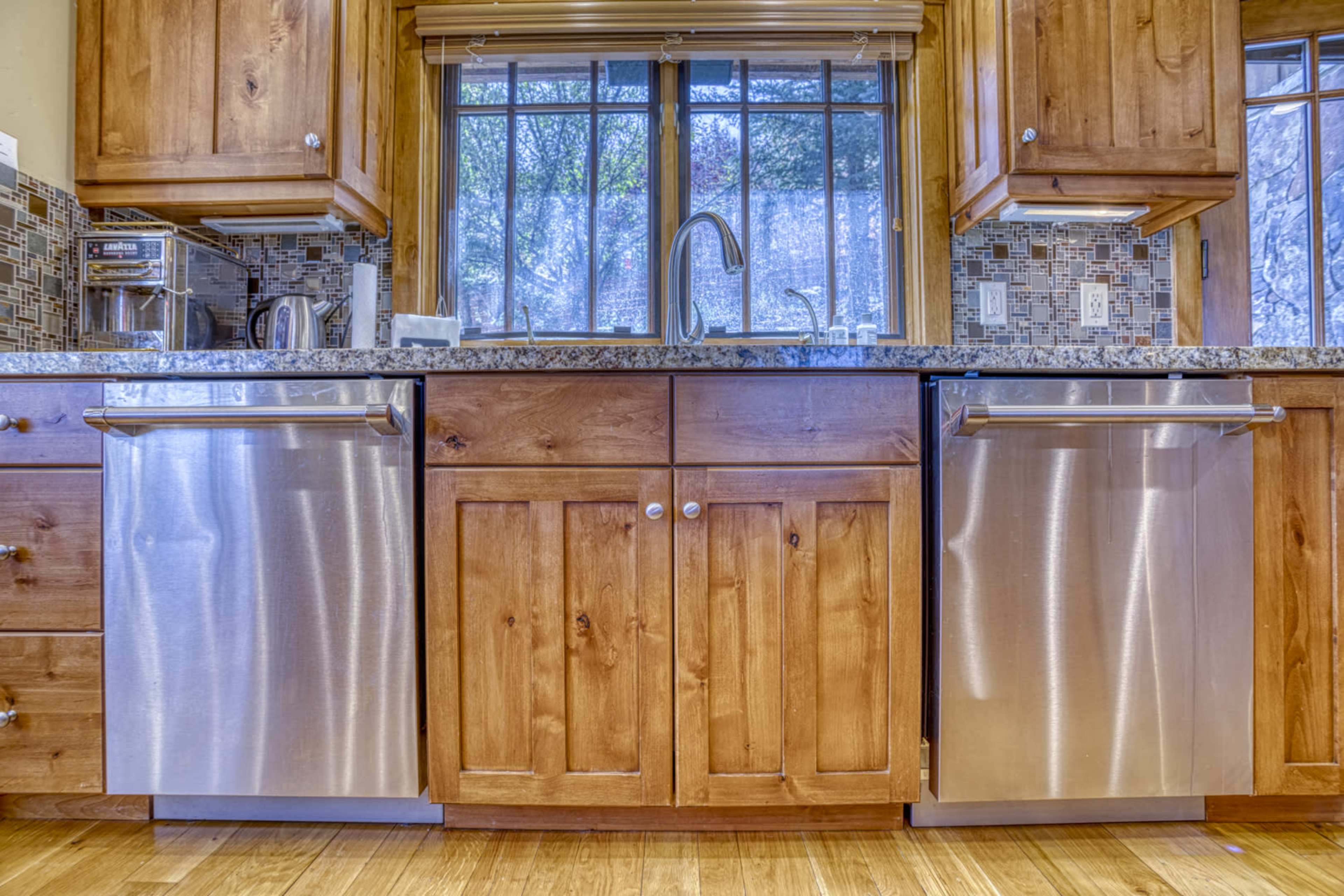 A kitchen with wooden cabinets, a granite countertop, and two stainless steel dishwashers under a window.