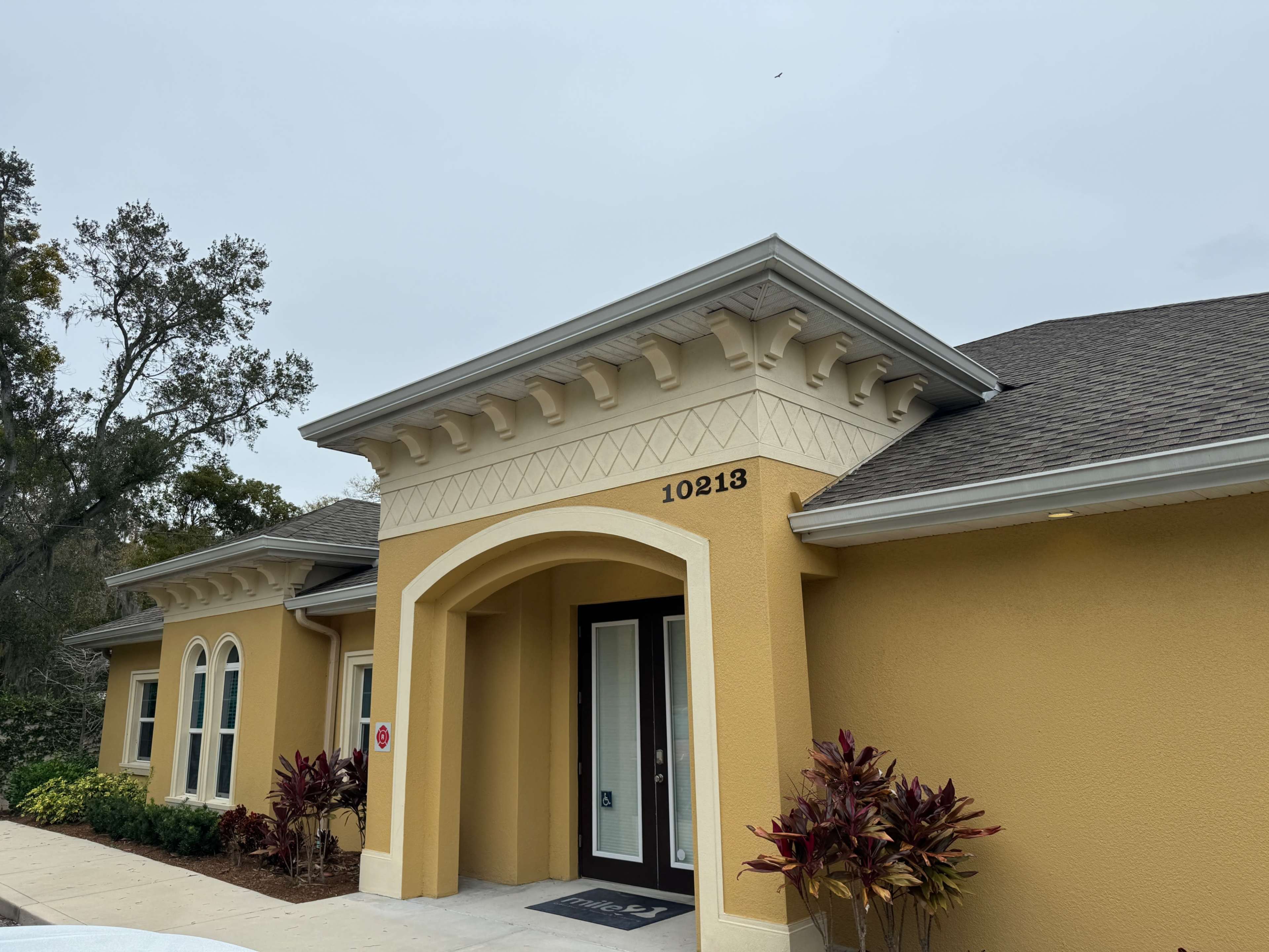 The image shows a yellow stucco house with a decorative entryway and the number 10213 displayed on the facade.