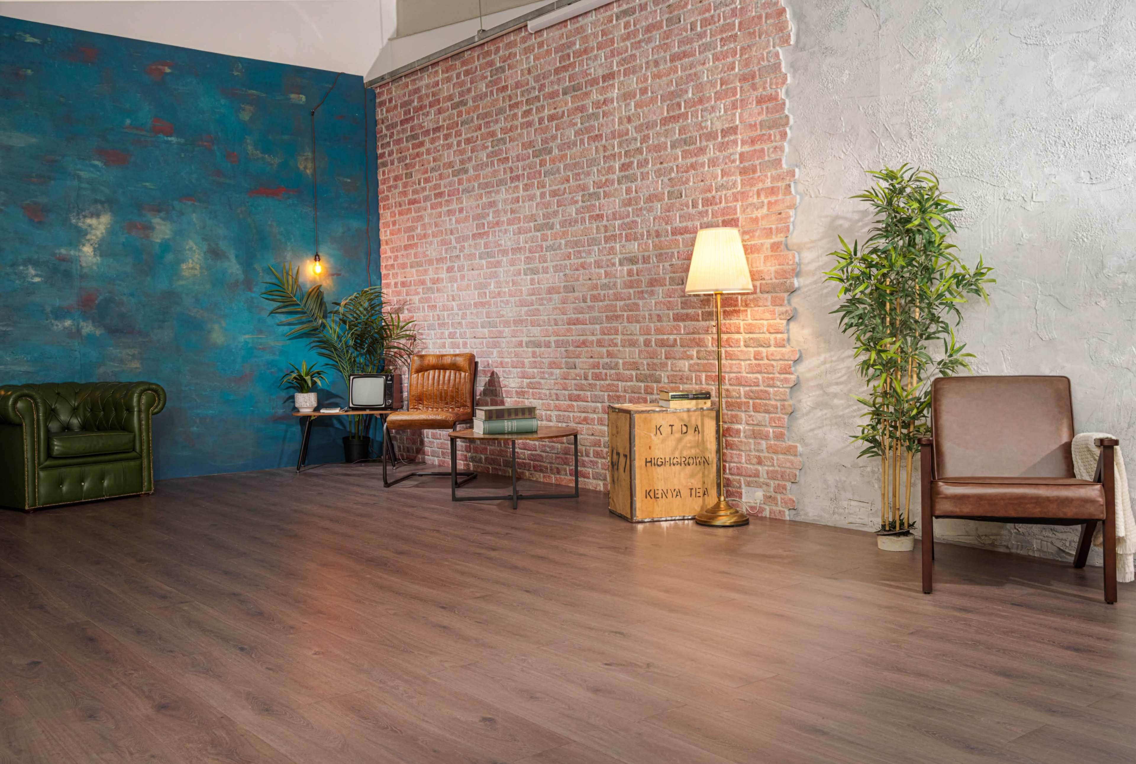 The scene features a modern interior with a blue and brick wall, wooden flooring, a floor lamp, various seating options, and a vintage television.