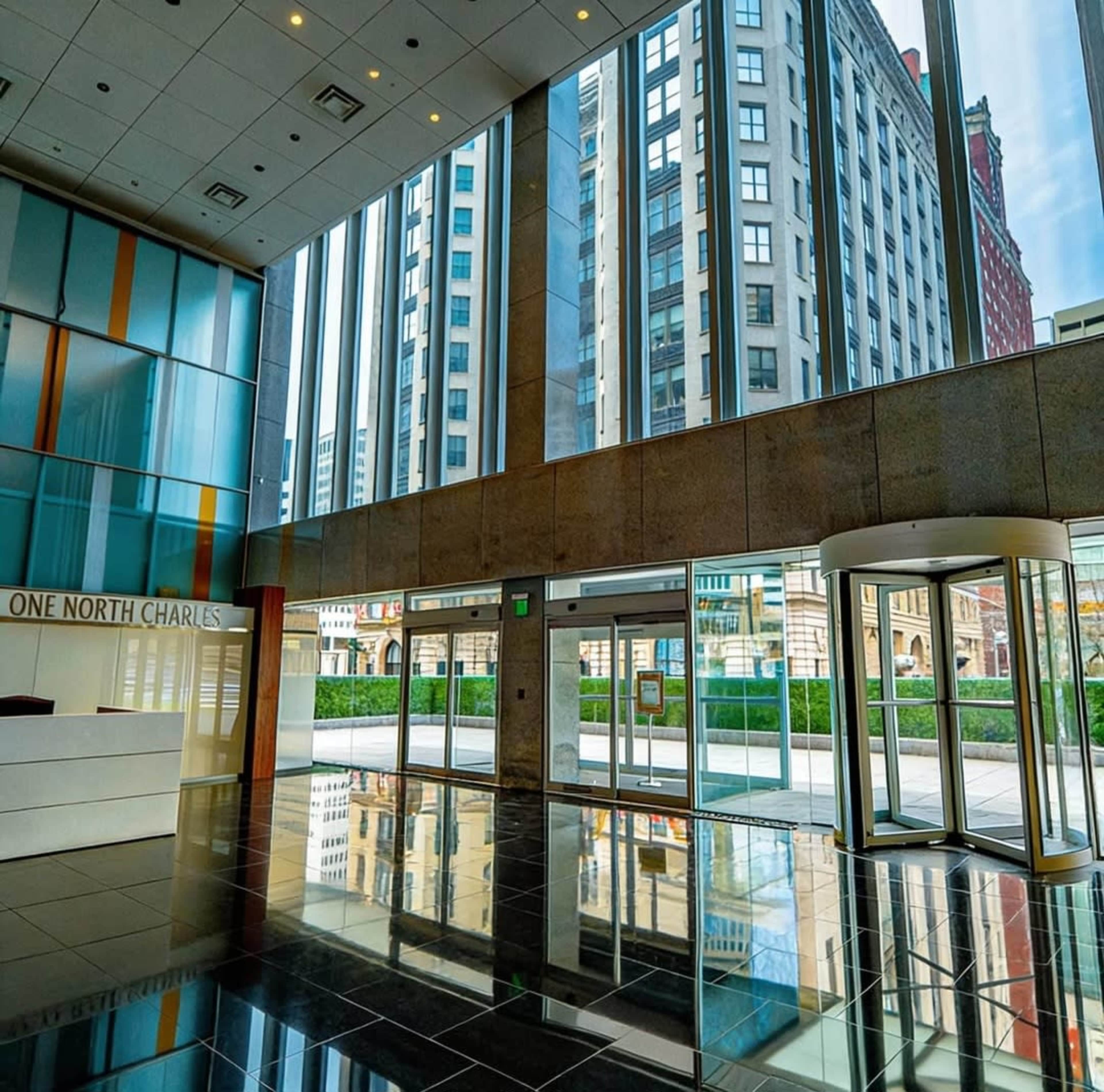The image shows a modern lobby with large windows reflecting city buildings and a revolving door.