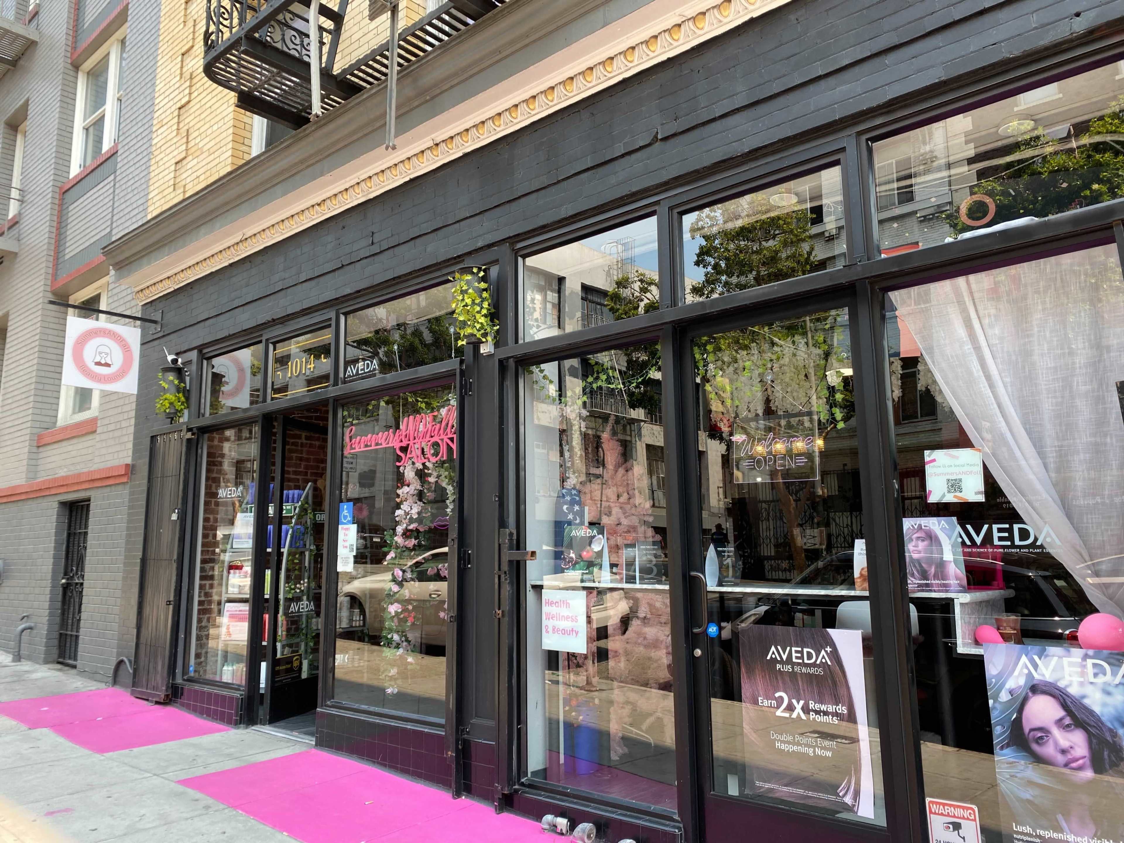 The storefront features a beauty salon with large glass windows, pink carpeting, and signage for Aveda products.
