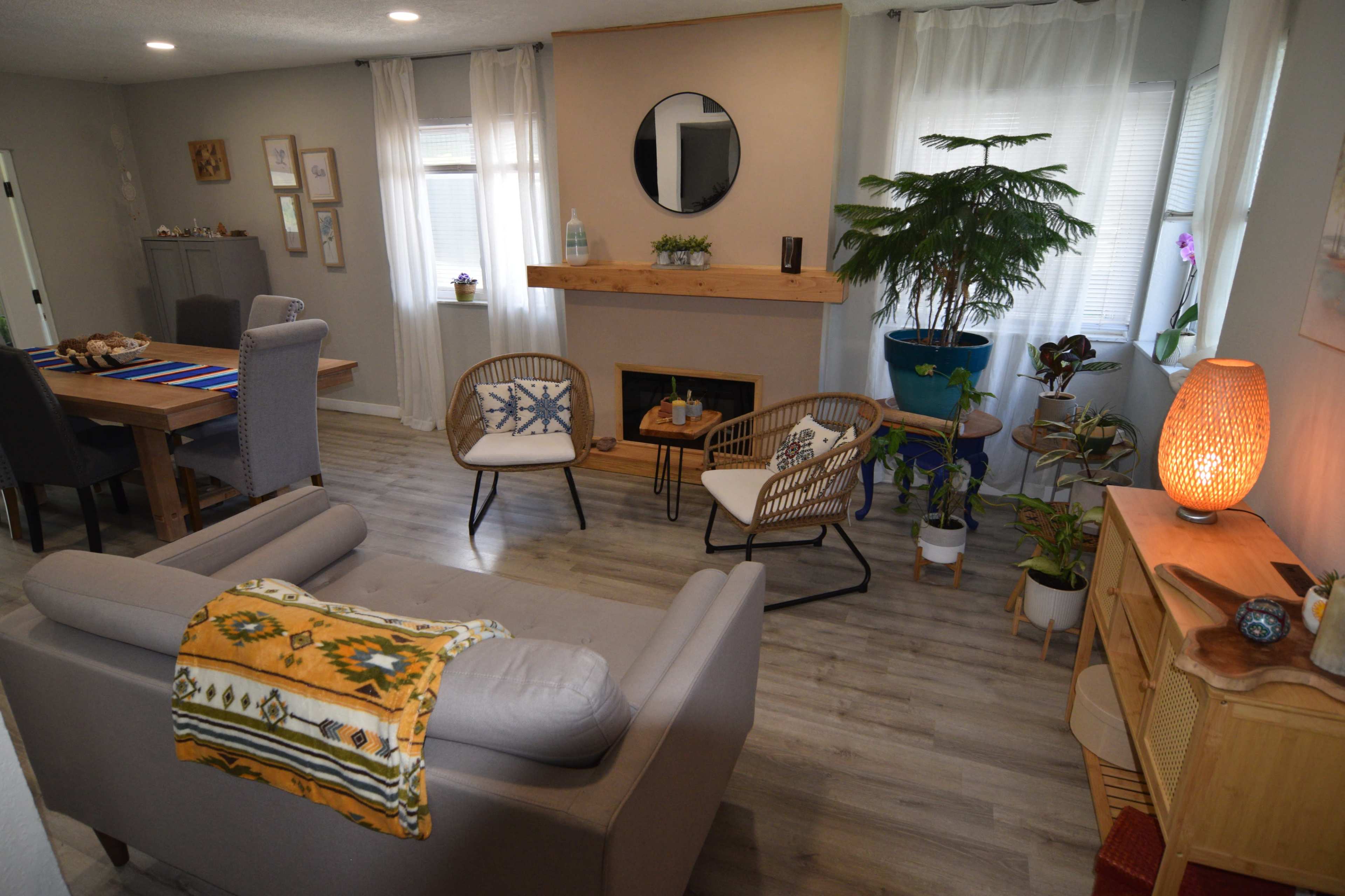 The image shows a cozy living room with a seating area, a fireplace, and various indoor plants.