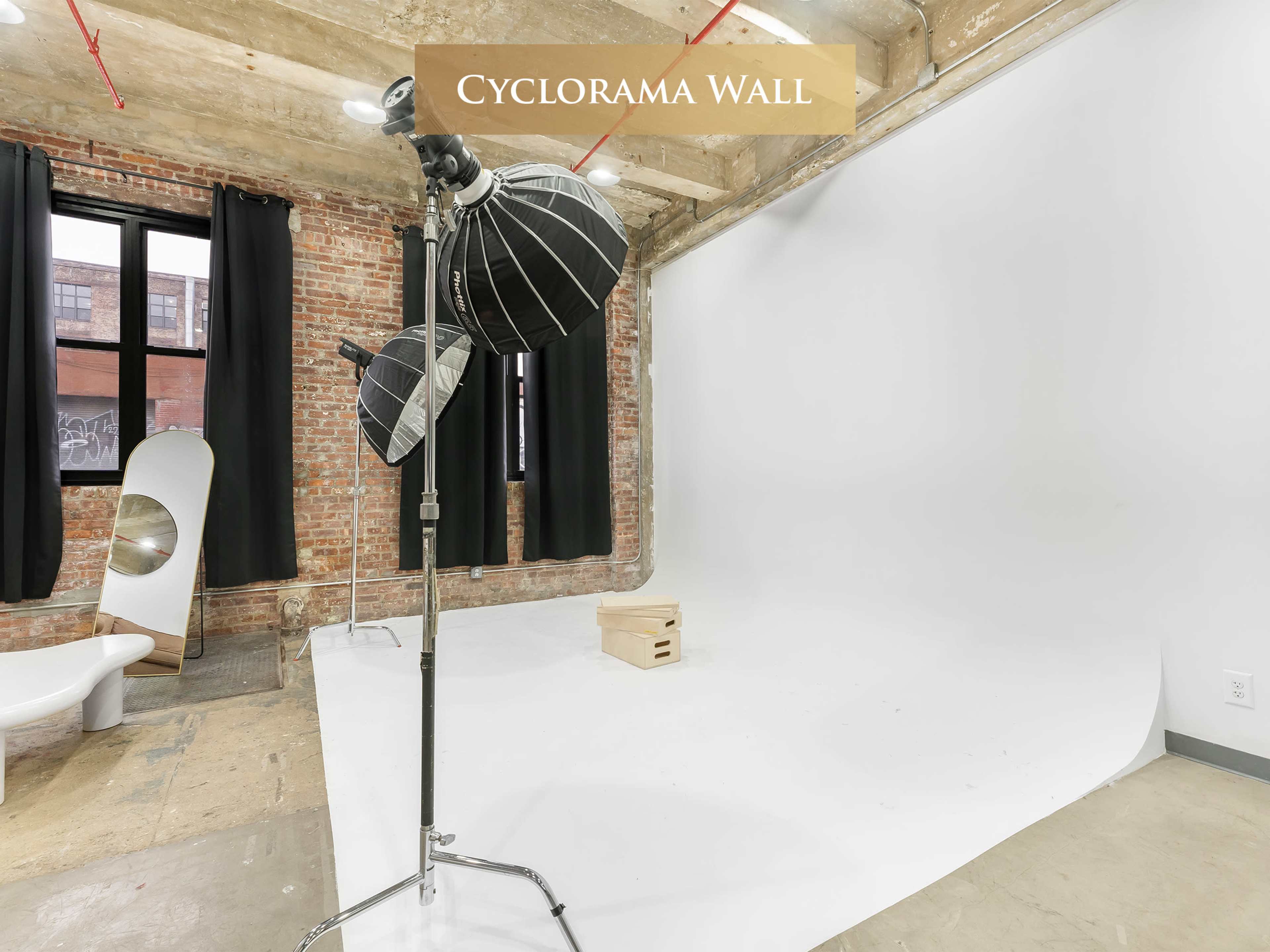 The image shows a photography studio with a cyclorama wall, three light stands, and a simple wooden crate on the floor.