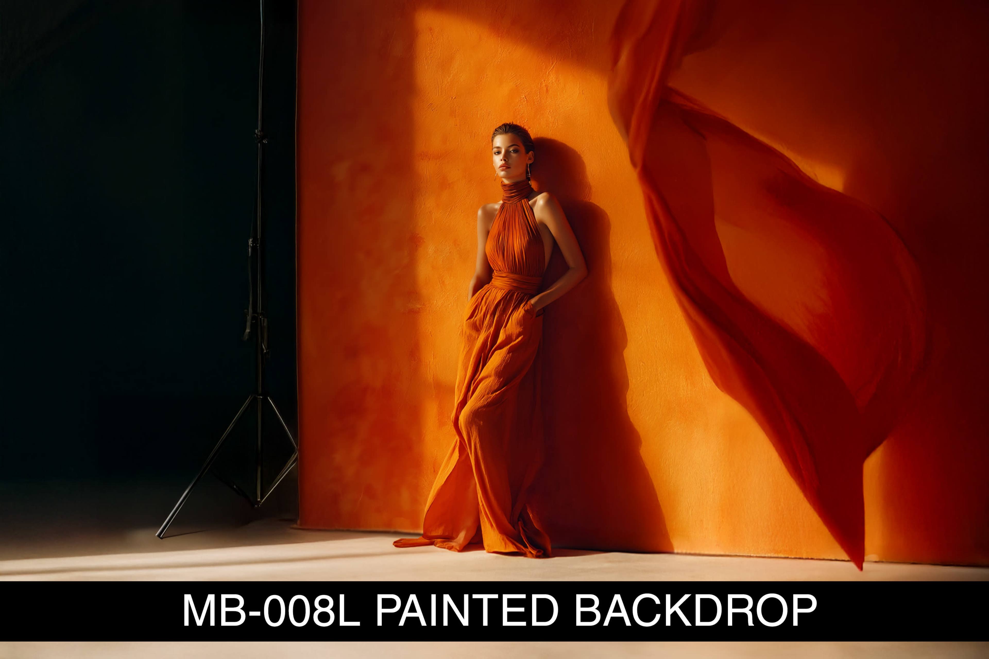 A model in an orange gown poses against a vibrant orange painted backdrop with a flowing fabric accent.