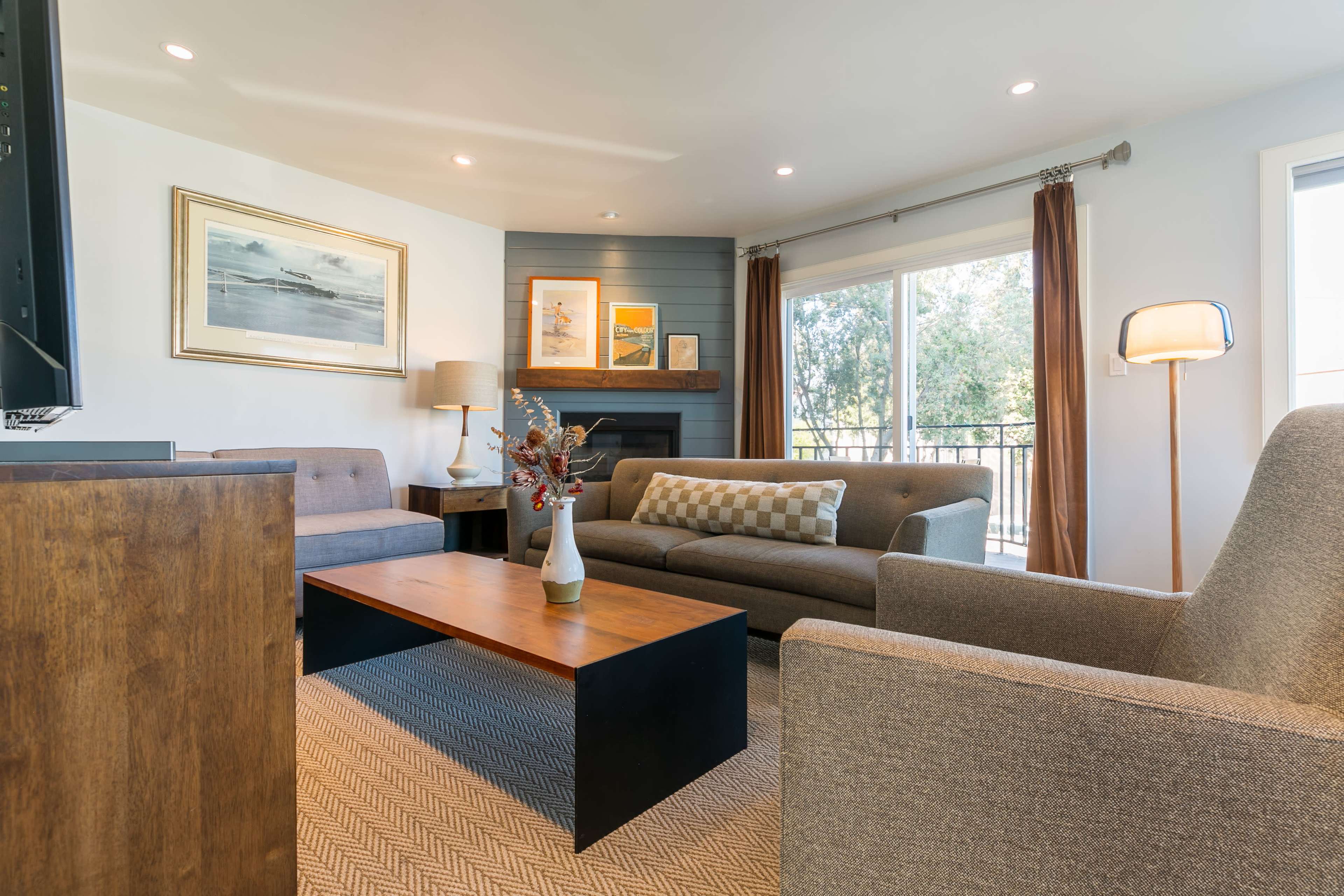 A modern living room features a neutral color palette with a gray sofa, two armchairs, a wooden coffee table, and artwork on the walls.