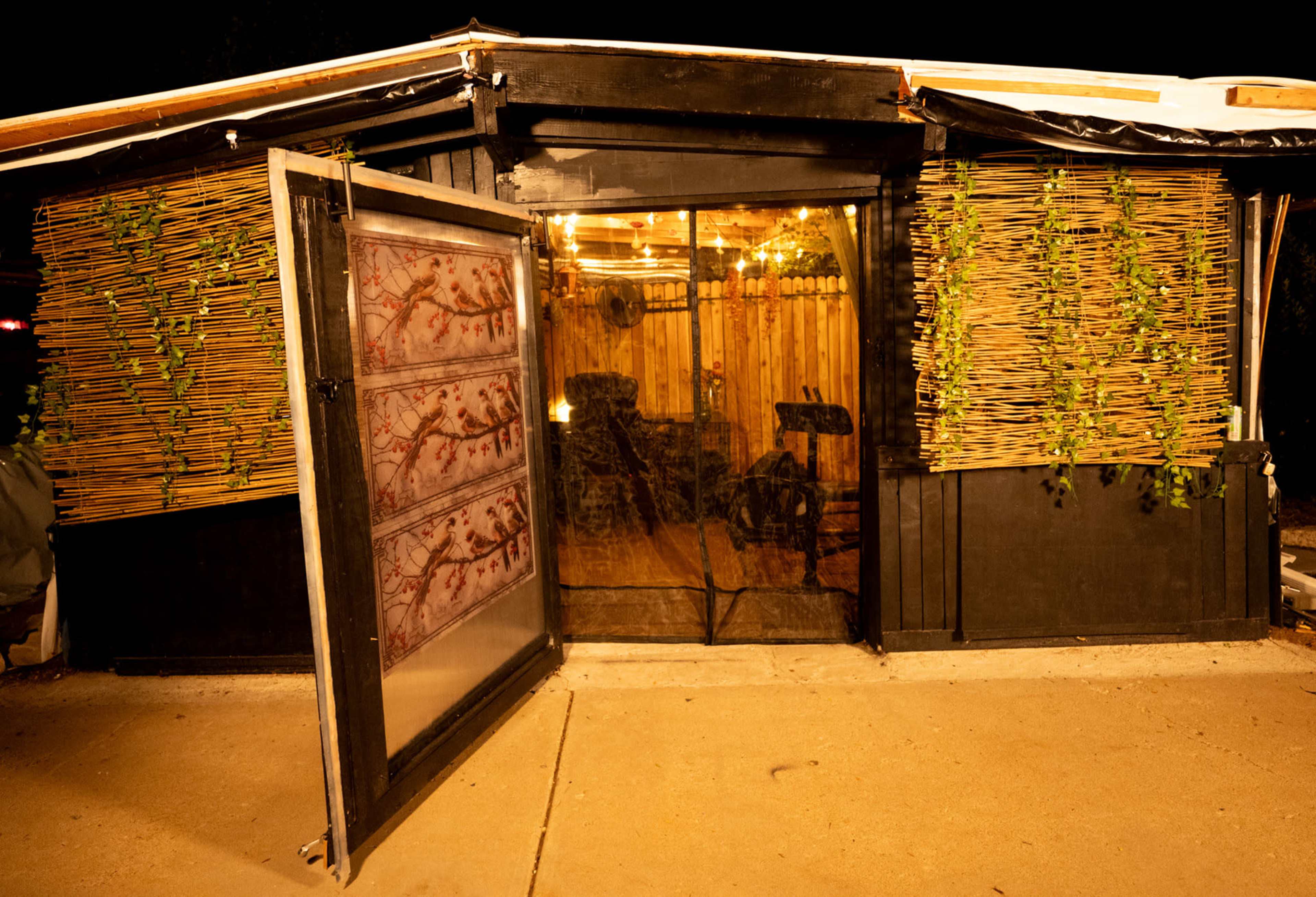 A partially open door leads to a dimly lit structure adorned with decorative bamboo and plants on its exterior.