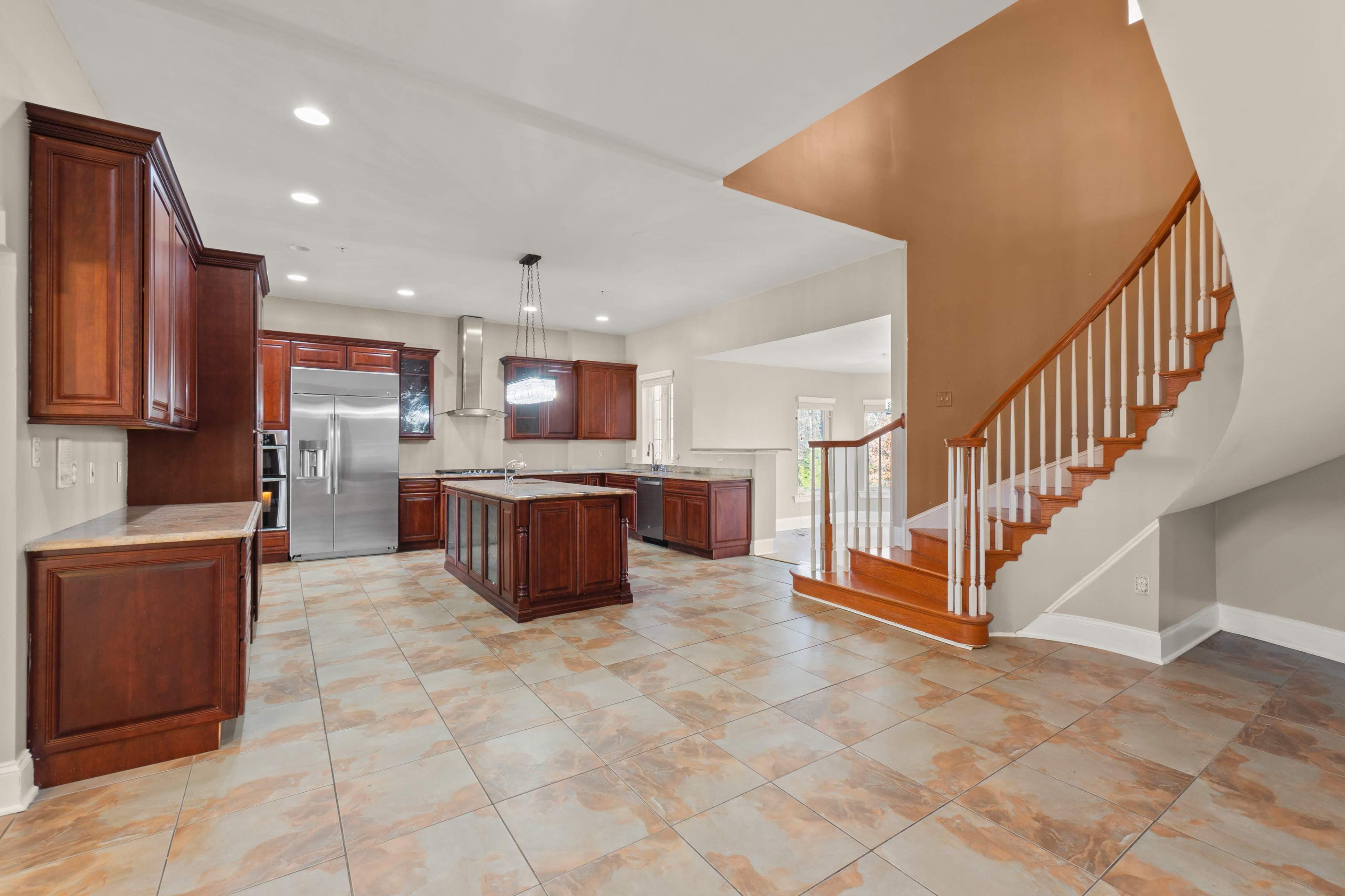 A spacious kitchen with dark wood cabinetry, a large island, and a staircase nearby leading to an upper level.