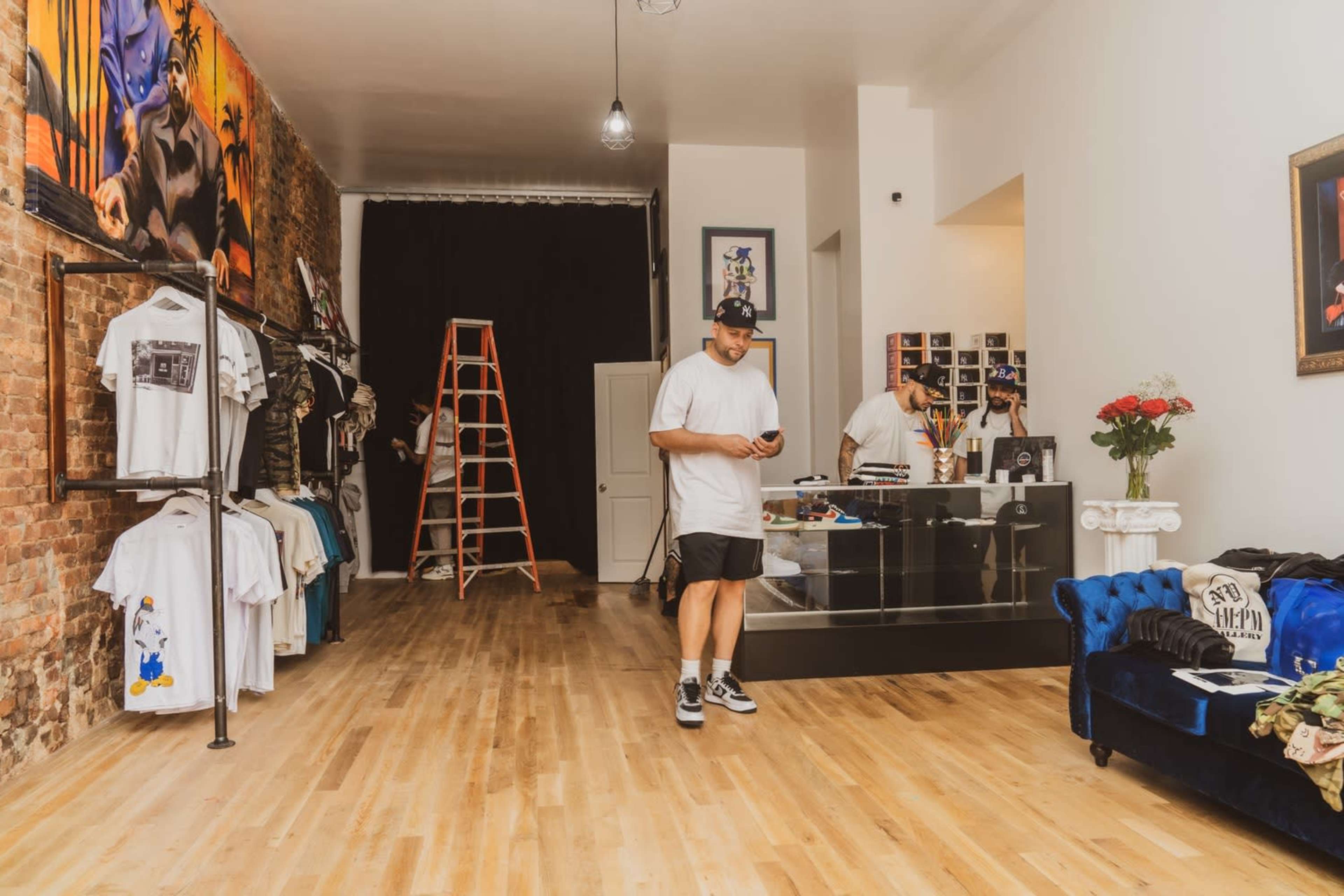 A person stands inside a clothing store with exposed brick walls, displaying various apparel on racks and a counter with items visible.