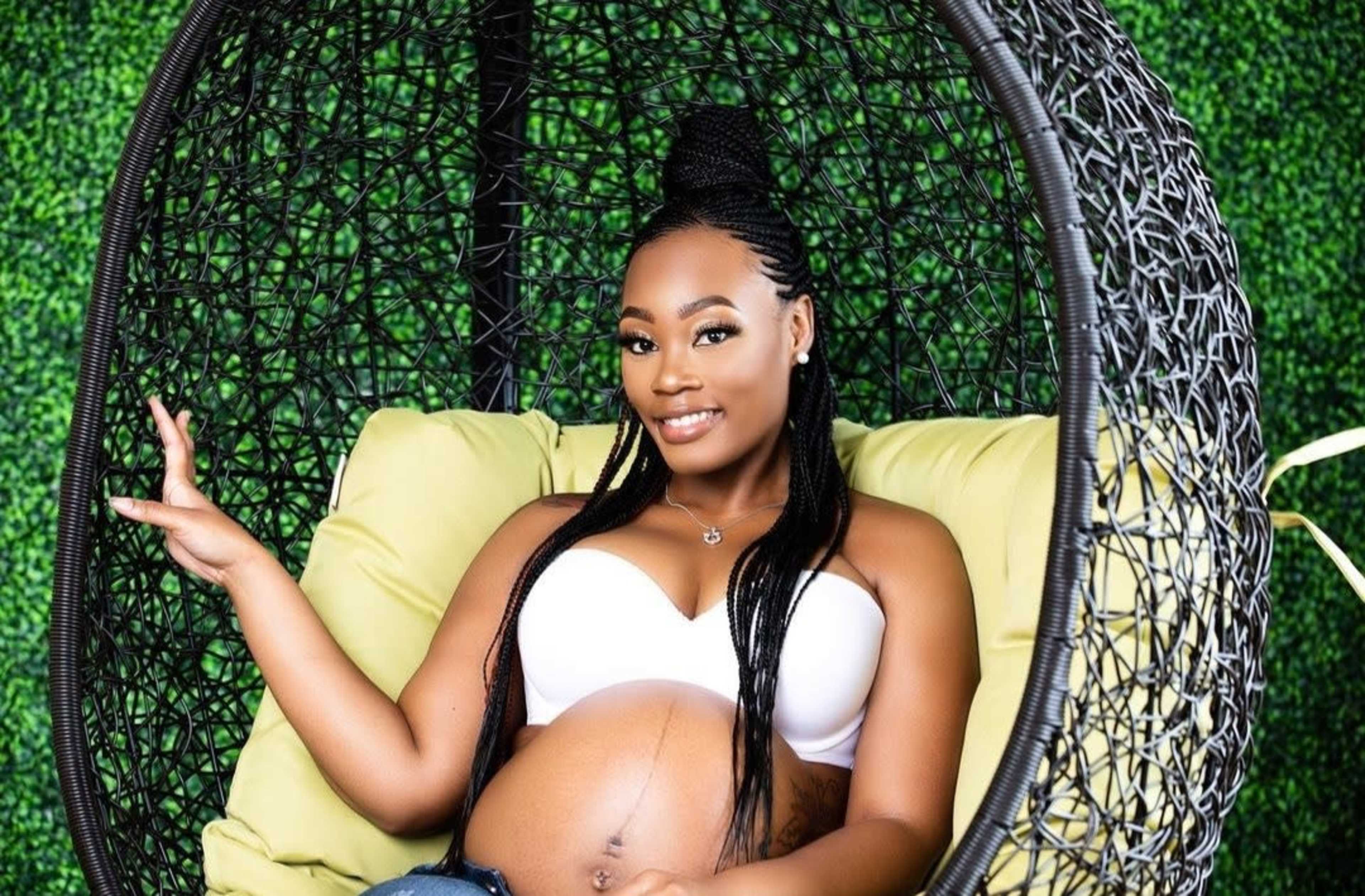 A pregnant woman sits in a hanging chair against a backdrop of green foliage.