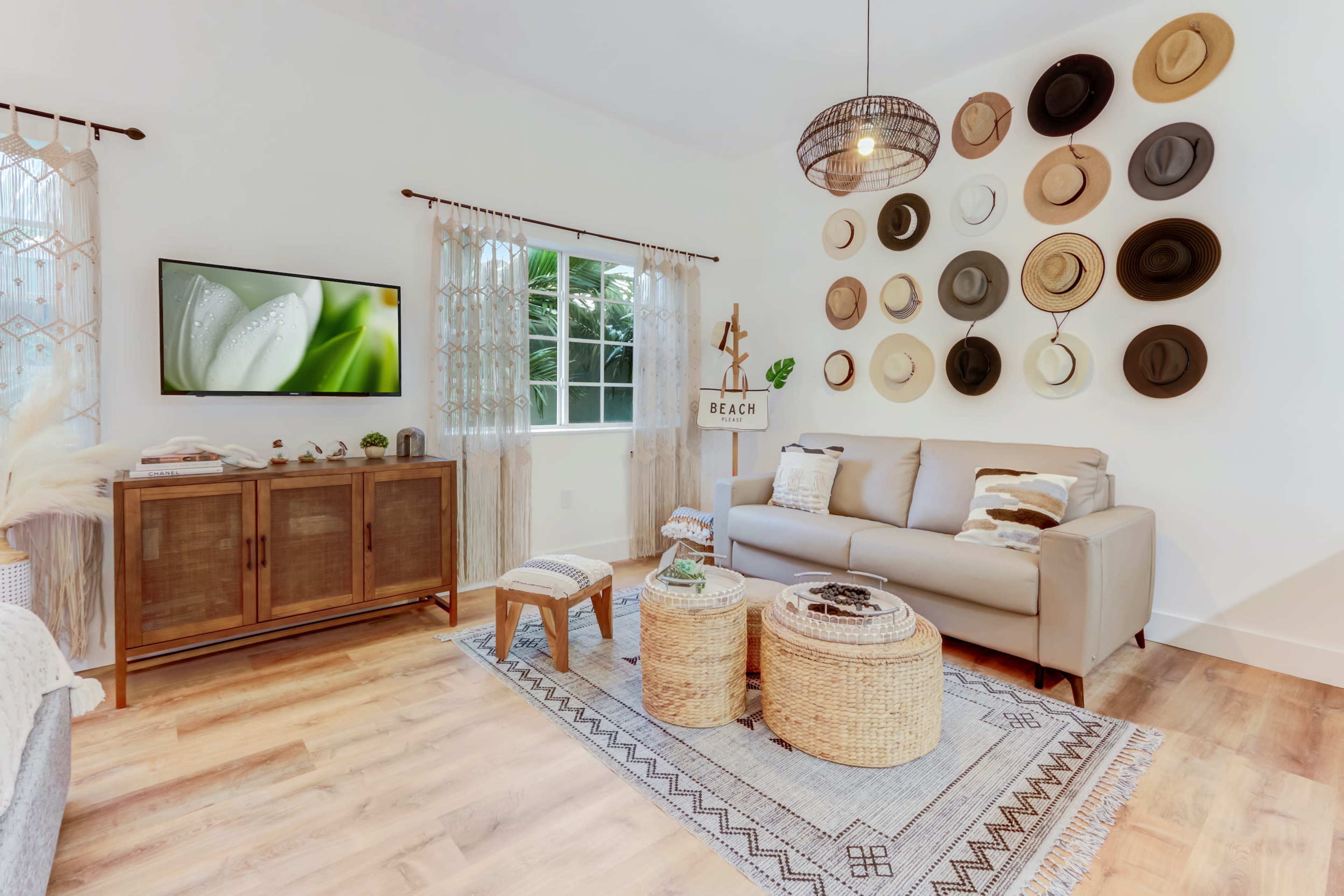 The living room features a light-colored sofa, a wooden media console, a hat display on the wall, and a woven rug with a coffee table and decorative accents.
