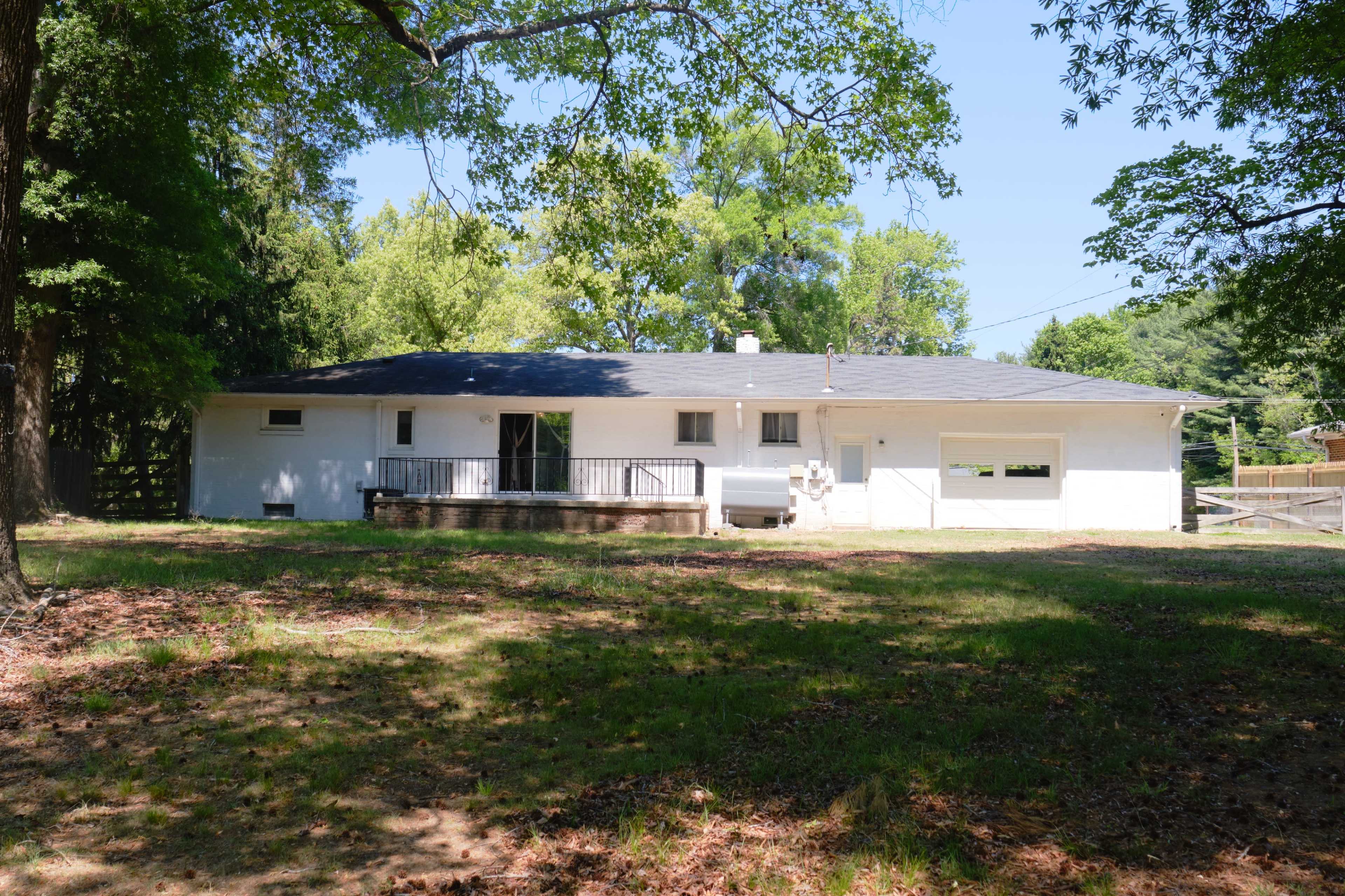 The image shows a single-story white house surrounded by trees, with a concrete front porch and a garage on the side.
