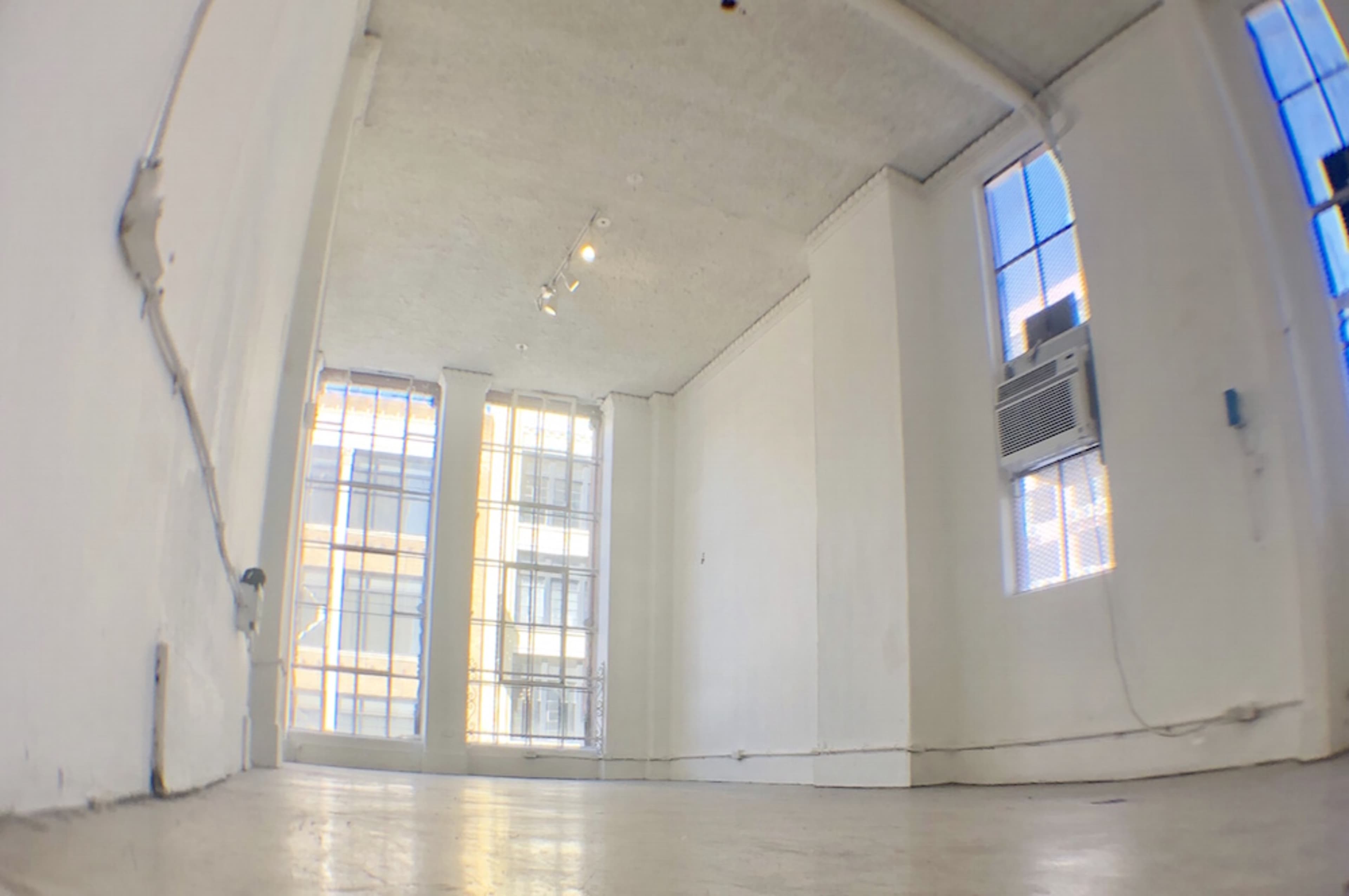An empty, well-lit room with large windows and an air conditioning unit.