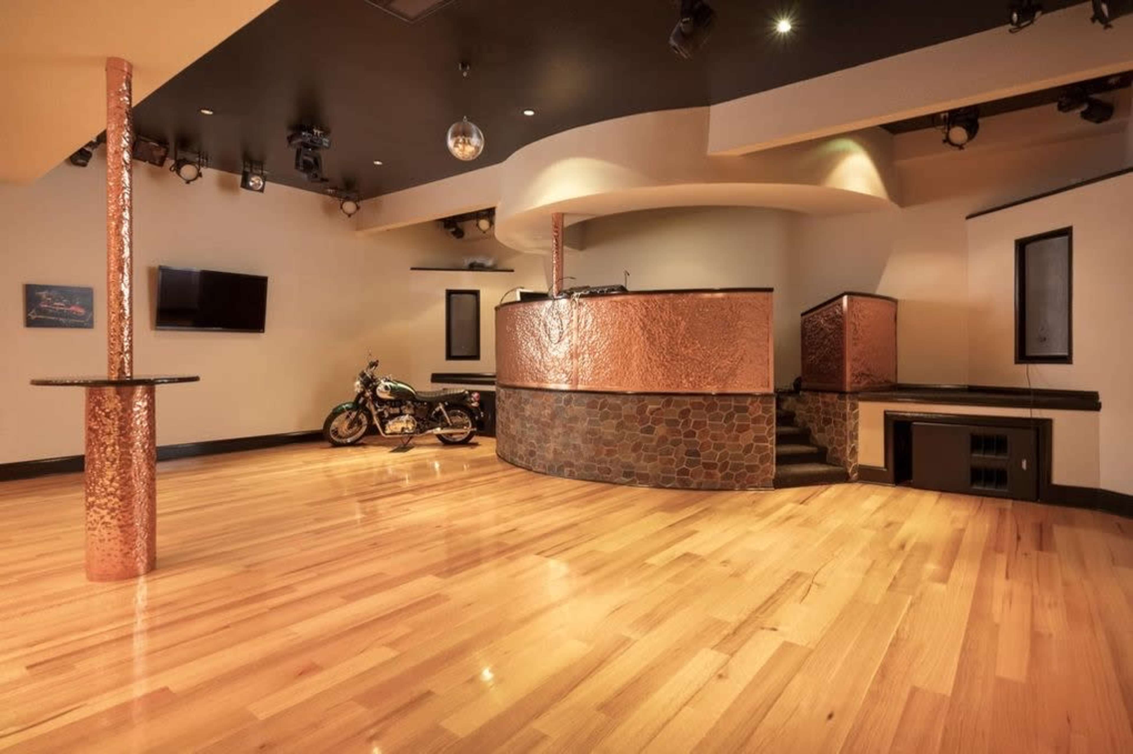 A modern lounge area with a wooden floor, a curved copper bar, and a motorcycle parked beside it.