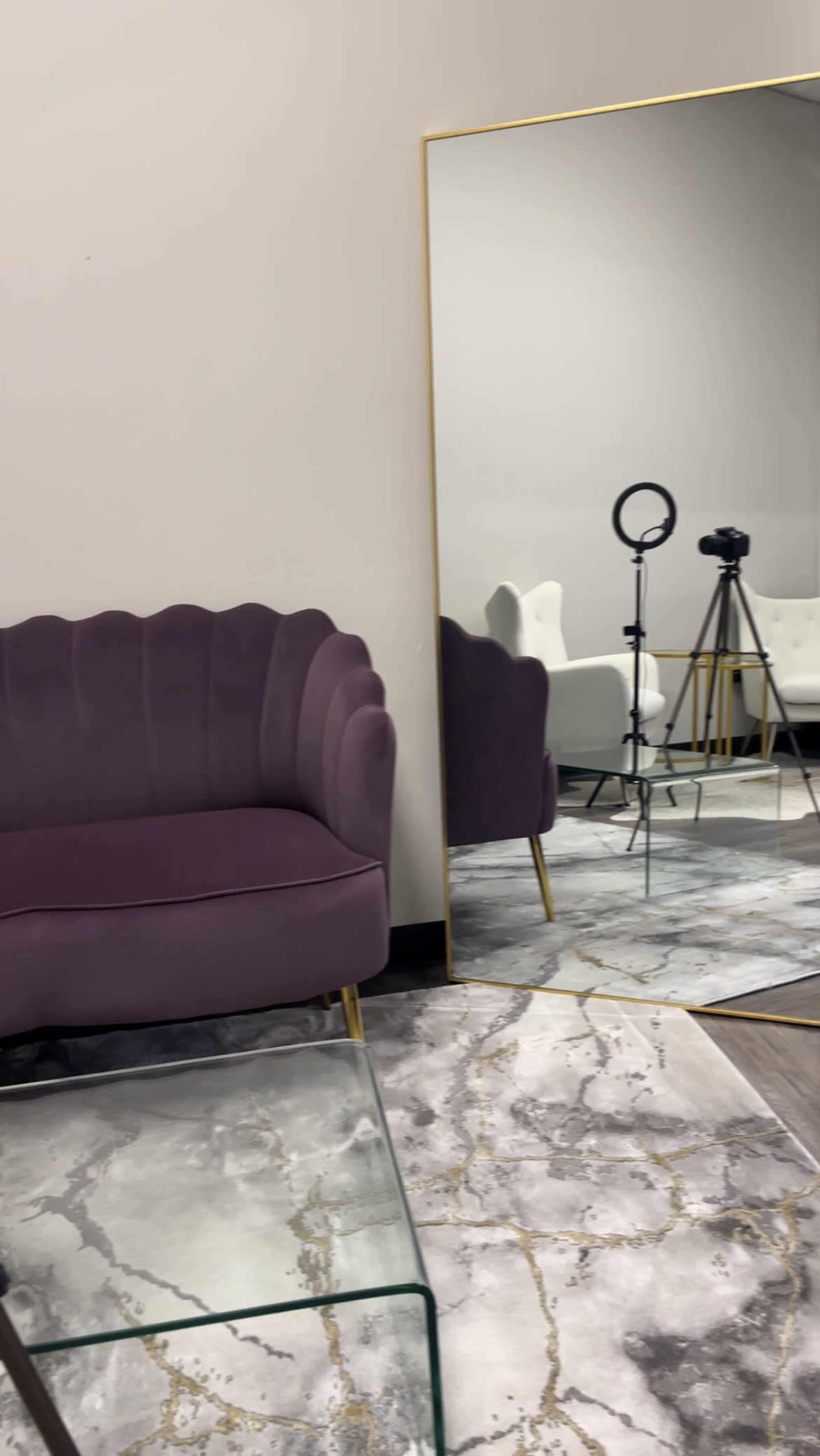 A purple velvet couch next to a large mirror, with a camera tripod and a ring light reflected in the mirror.