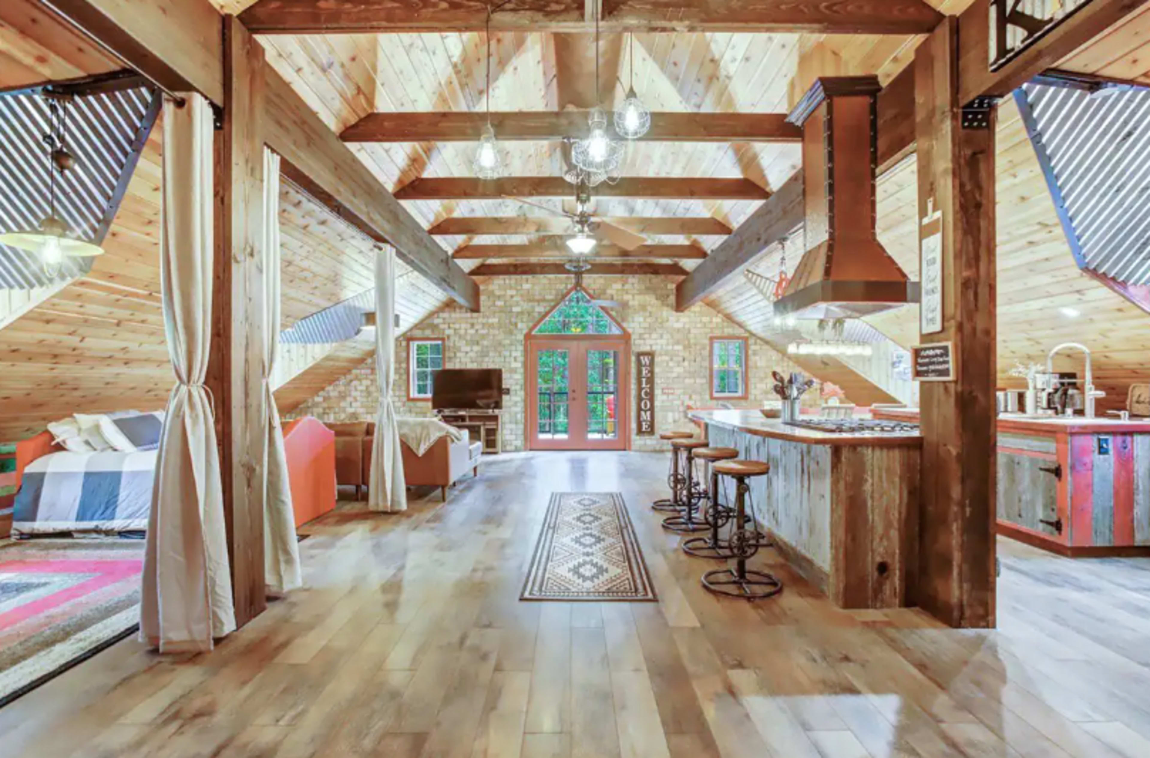 An open-concept, rustic-style cabin interior with wooden beams, a kitchen area, and a living space featuring a large window.