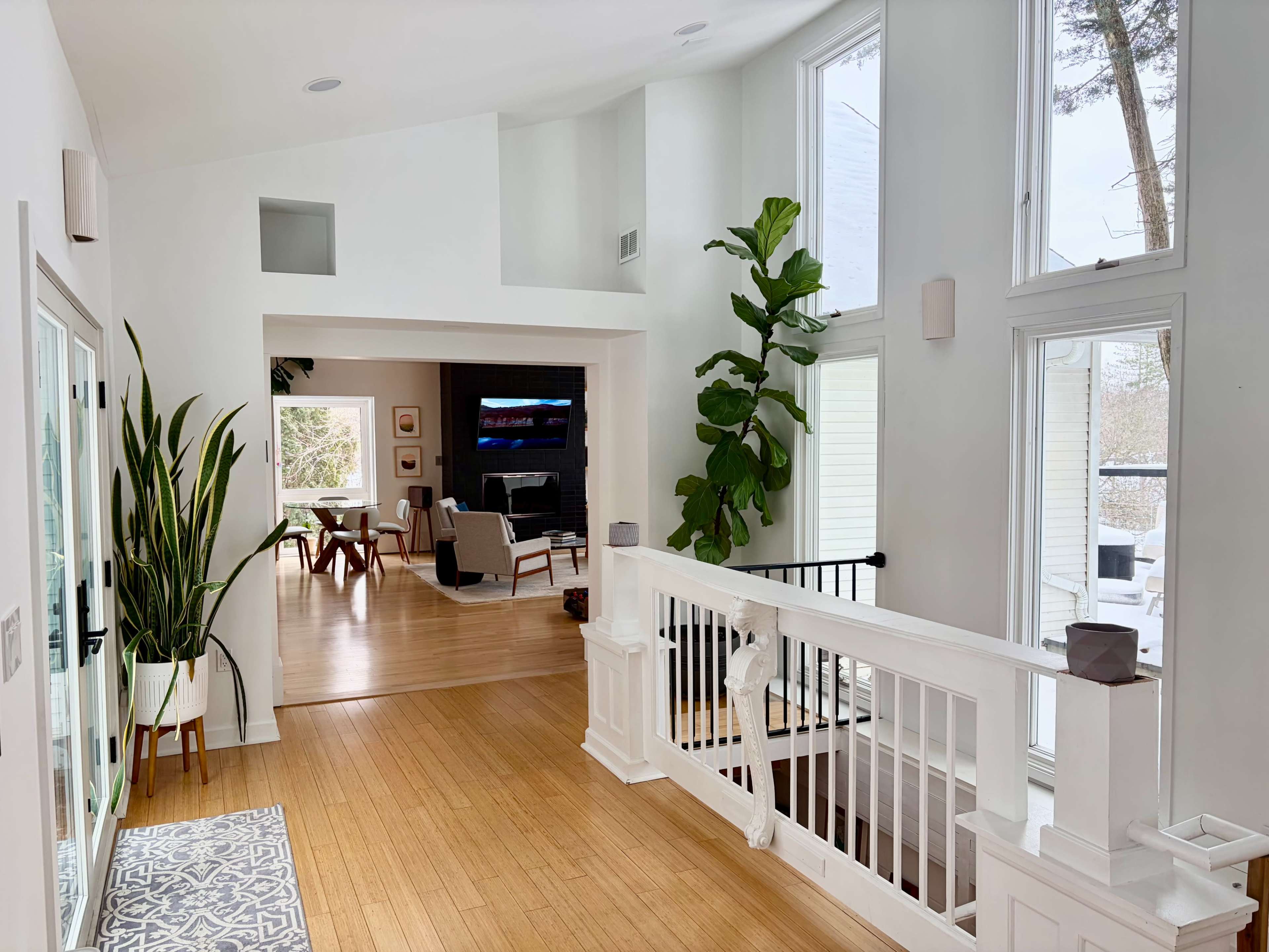 A bright, modern hallway features large windows, bamboo flooring, and a view of an adjacent living area.