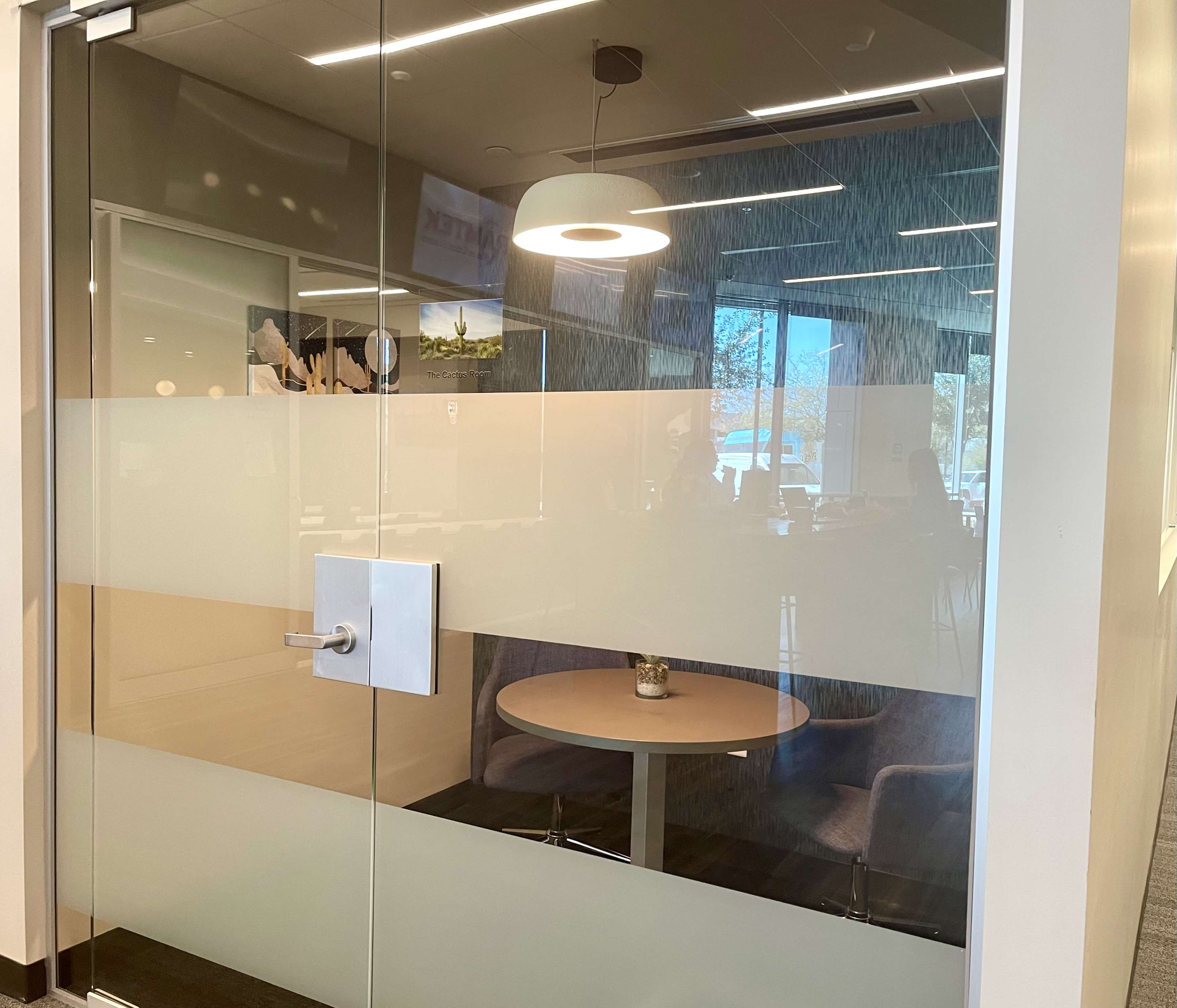 A glass-walled conference room with a round table and two chairs inside.