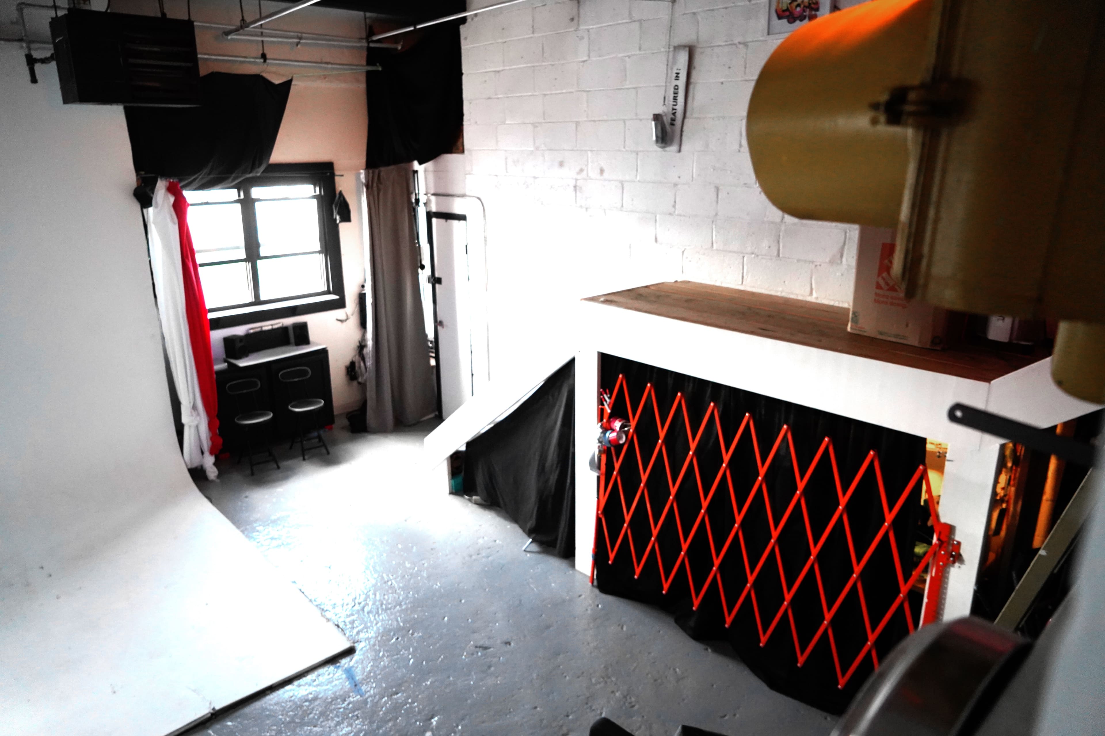 The image shows a photography studio with a white backdrop, a staircase, and an area enclosed by an orange safety gate.