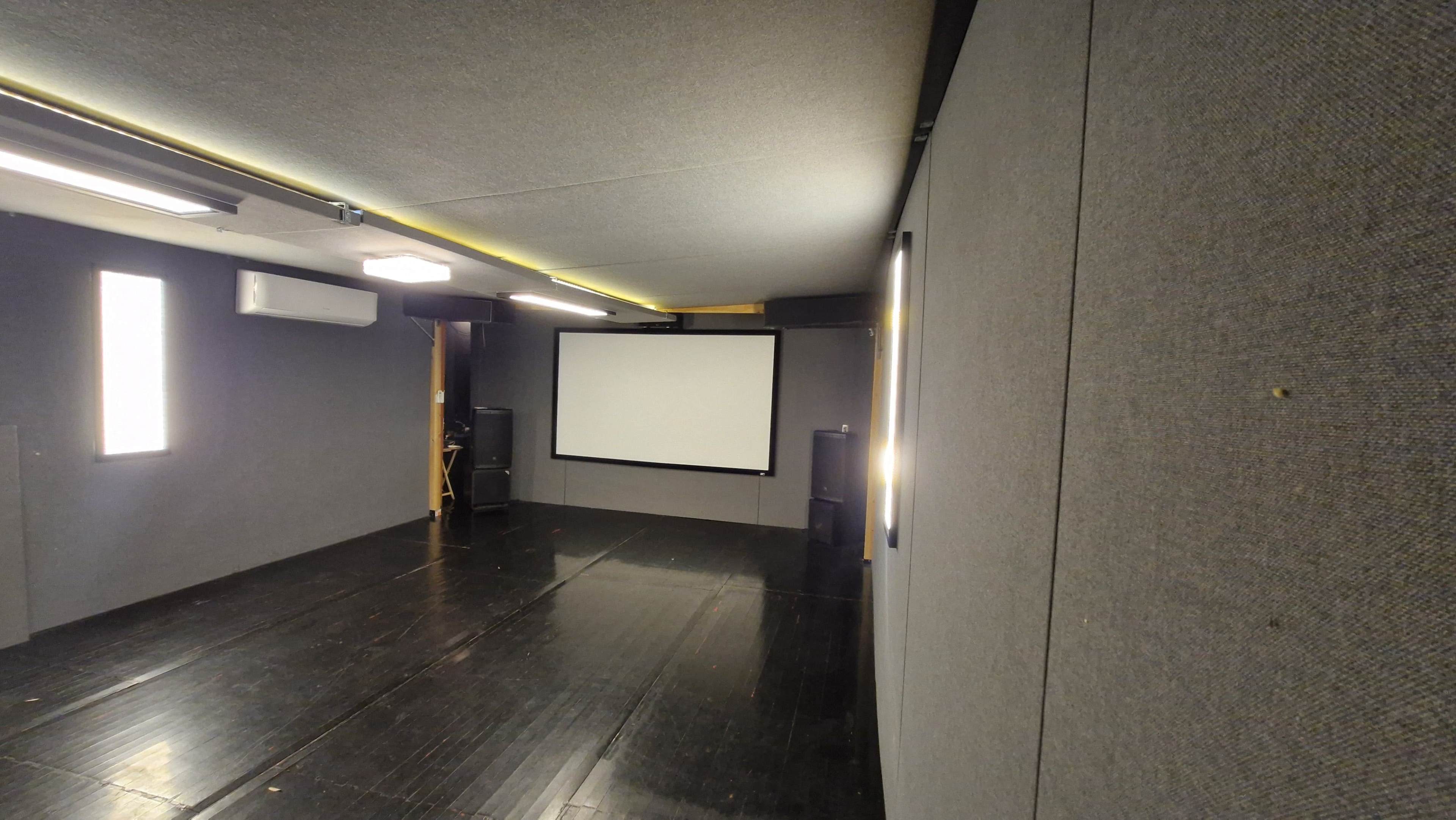 A sparsely furnished room with a large projector screen on one wall and minimal lighting.