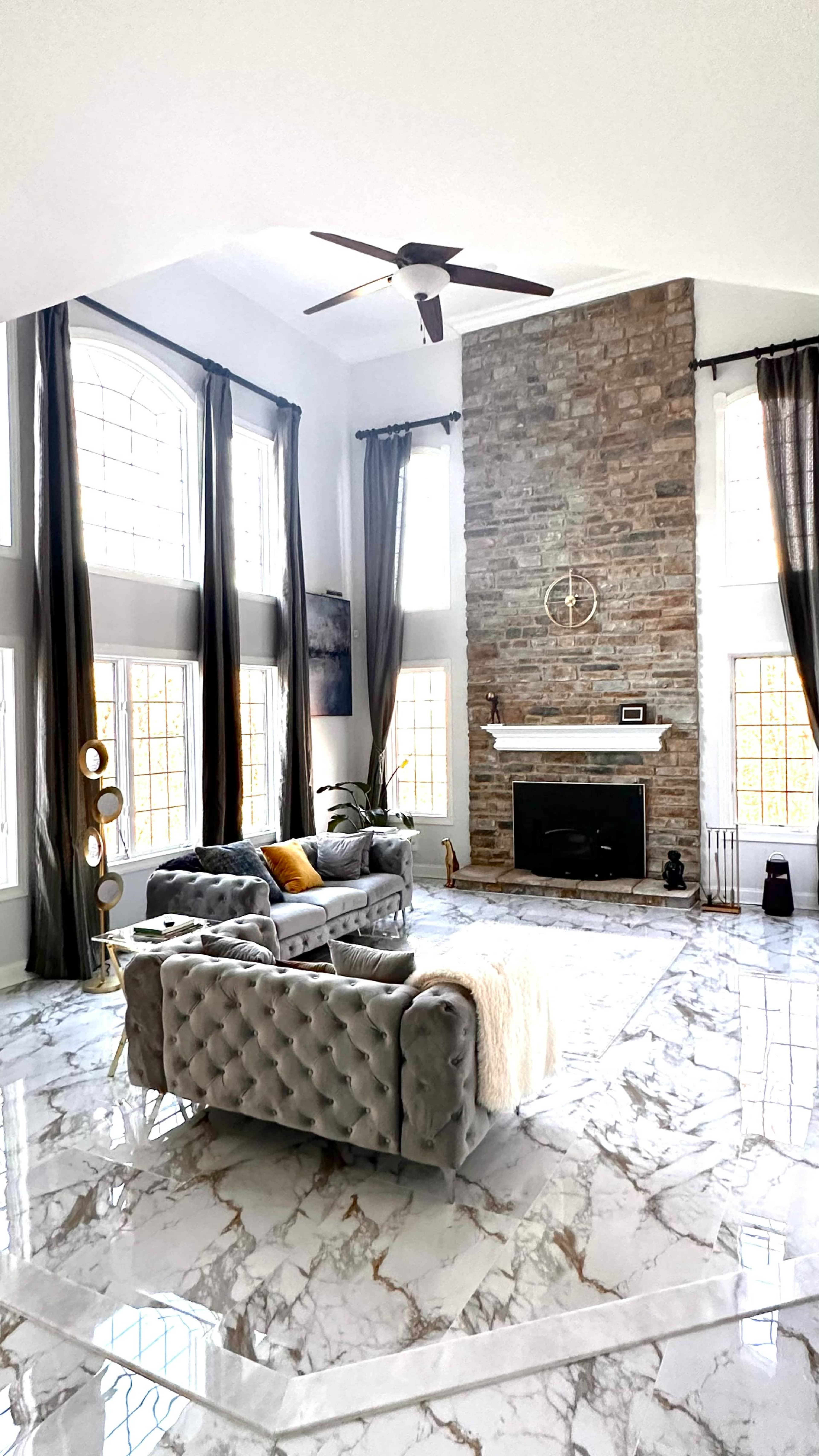 The spacious living room features a stone fireplace, large windows, marble flooring, and modern furnishings arranged for comfort.