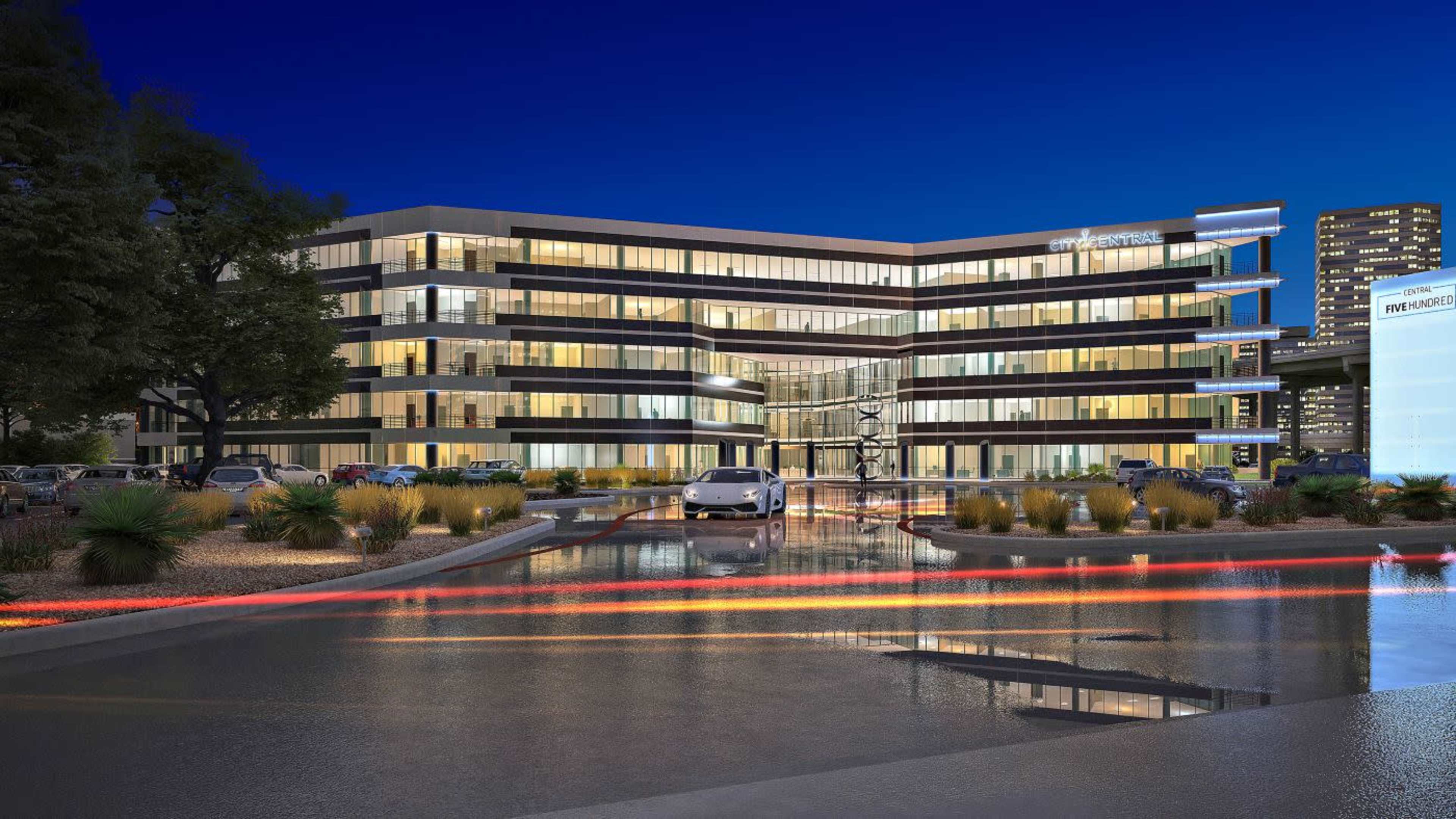 A modern office building with multiple glass façades is illuminated against a twilight sky, reflecting in a nearby water feature.