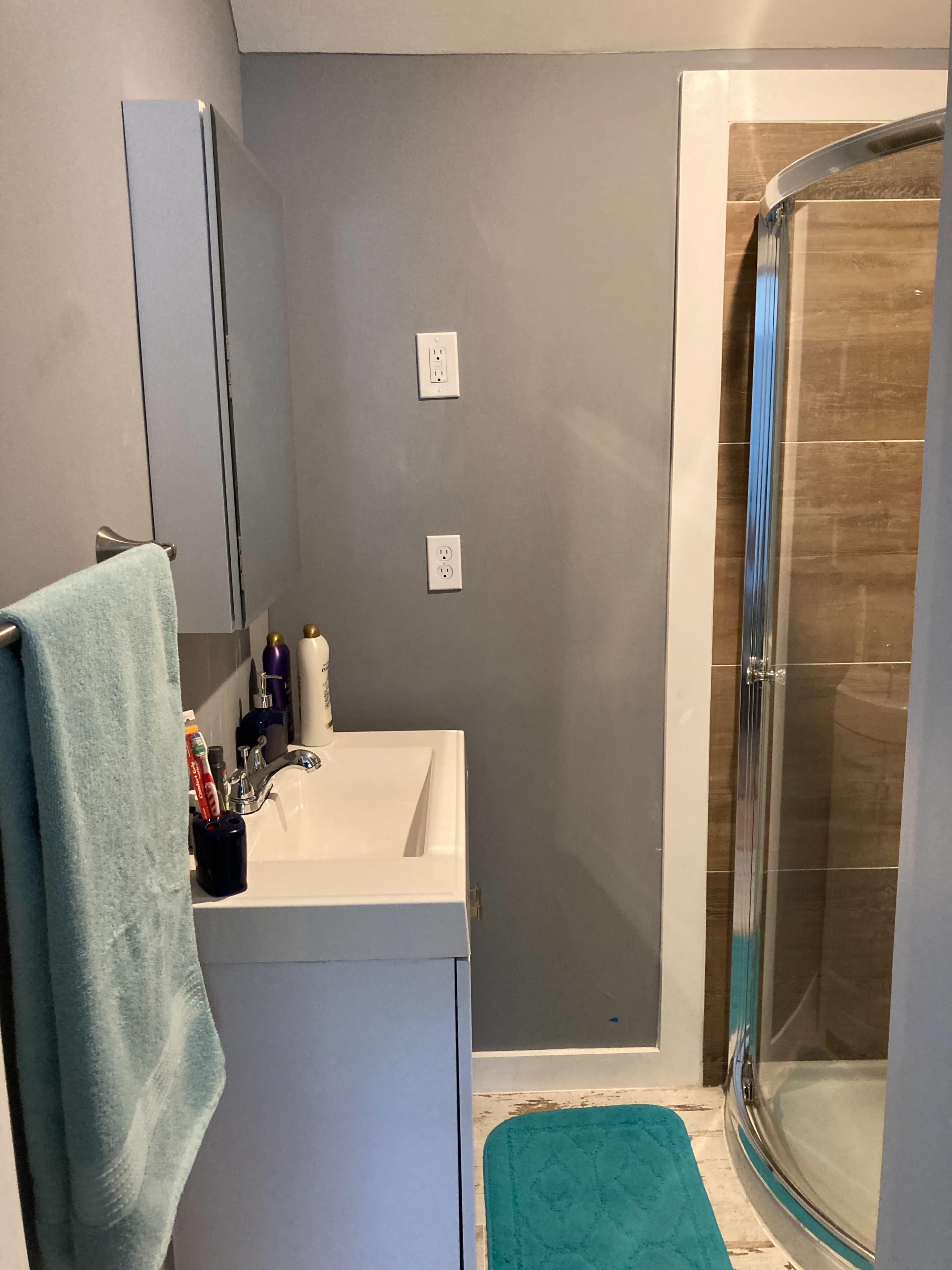 A bathroom with a single sink vanity, a wall-mounted mirror, and a shower enclosure on one side.