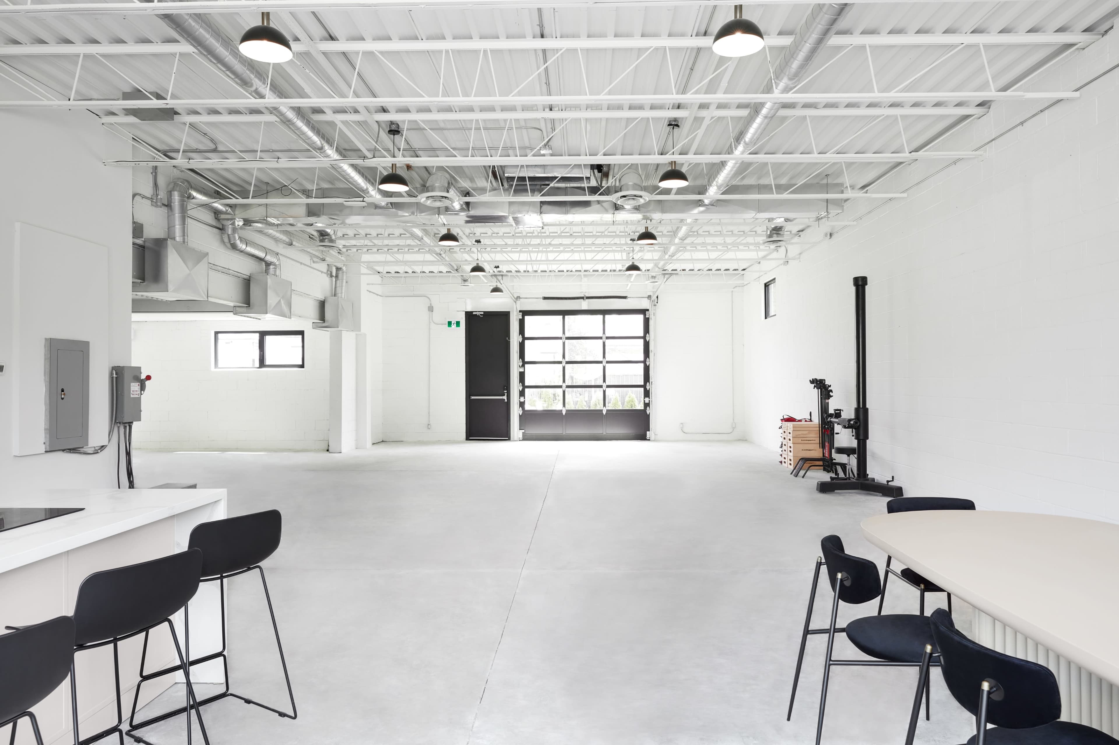 A spacious, empty interior of a modern industrial-style room with a kitchen area on the left and a large garage door at the far end.
