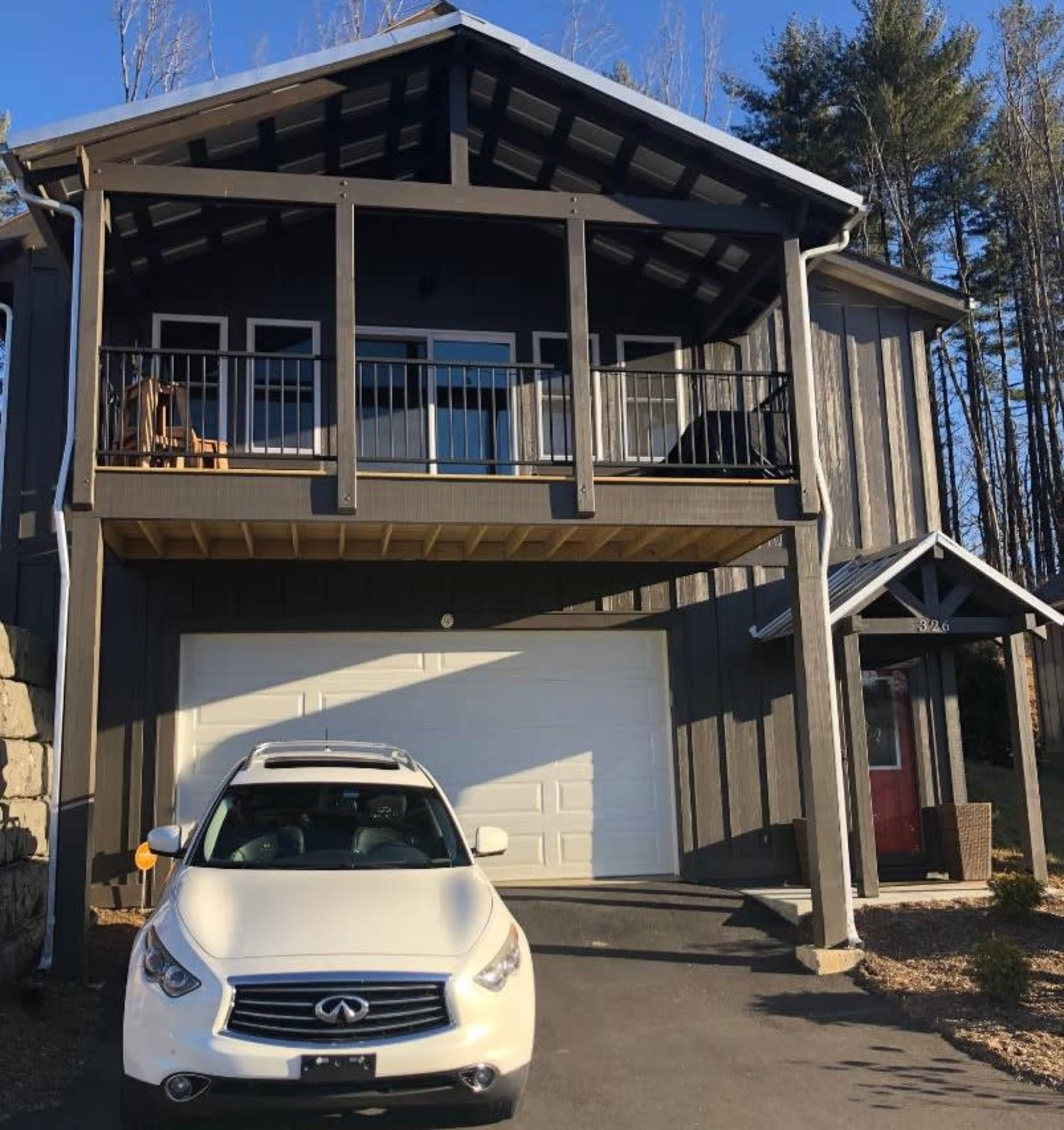 A two-story house with a balcony, featuring a white car parked in front of it and a garage door beneath the balcony.
