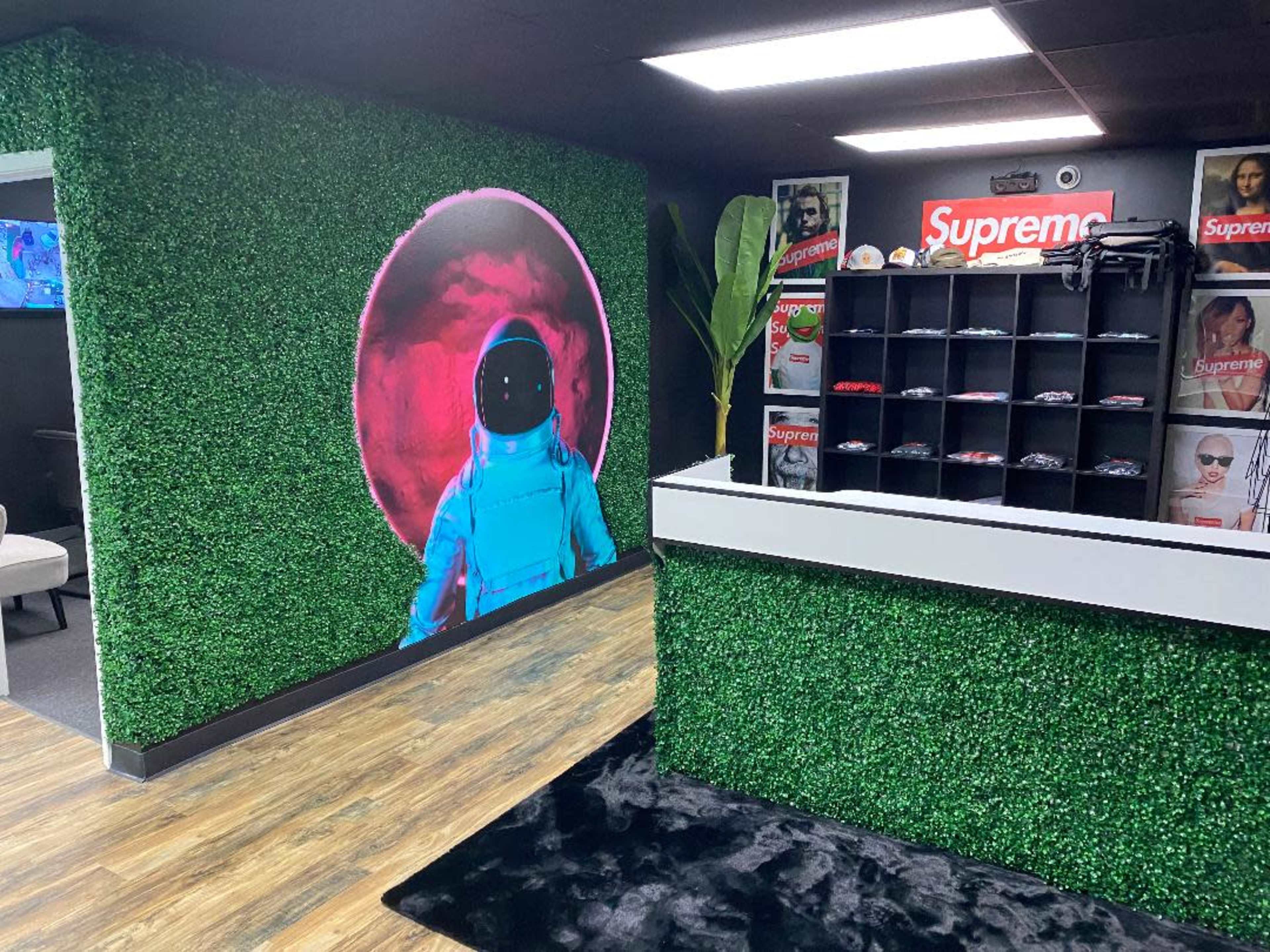 A retail space with green artificial grass walls, featuring a large astronaut mural and a counter displaying clothing items.