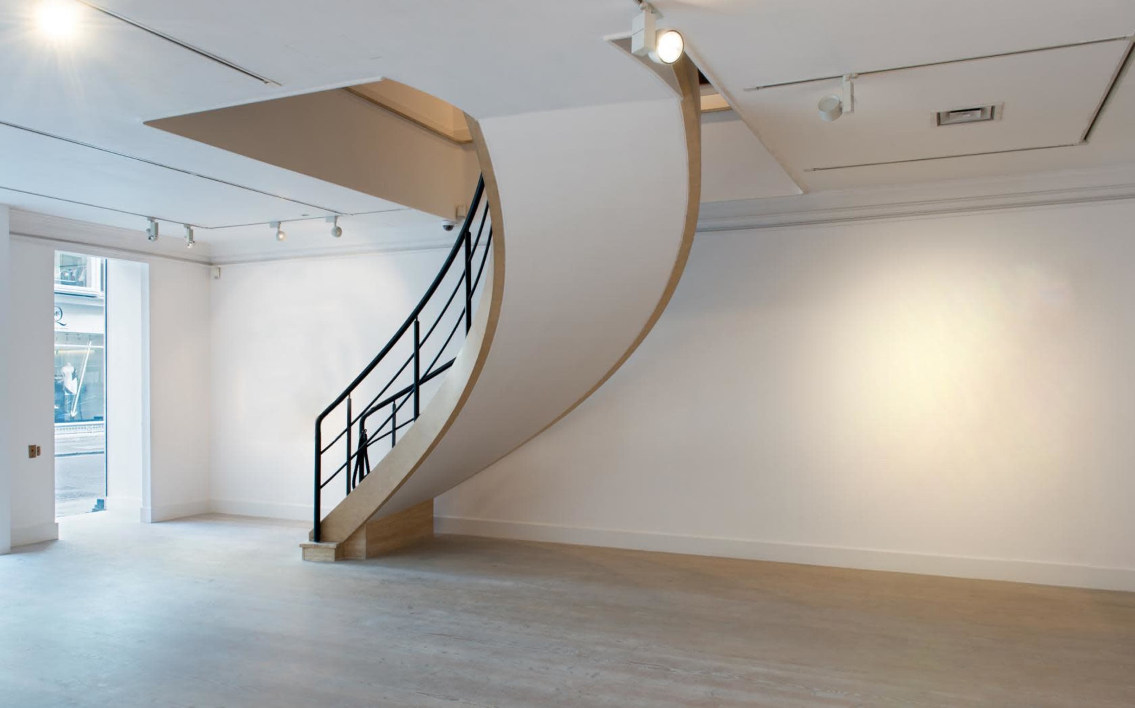 A modern interior space featuring a large, curving staircase against white walls, with a doorway visible to the left.